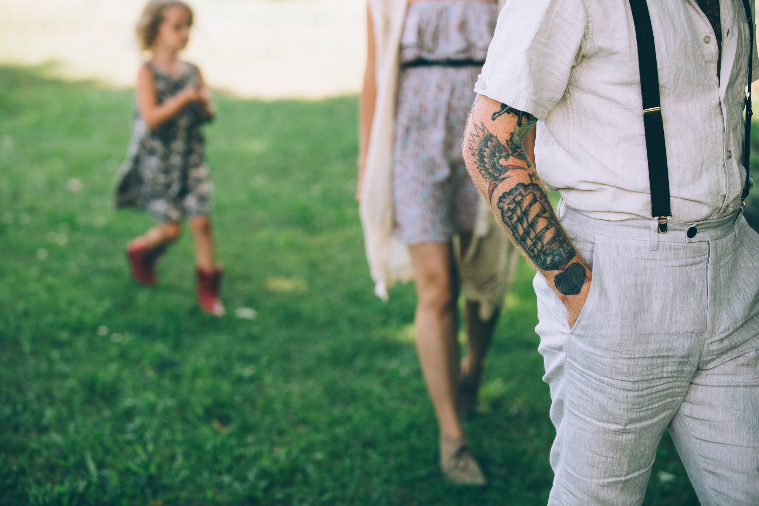 A close-up shot focusing on a tattooed arm of a person dressed in vintage attire, with blurred figures walking in the background.