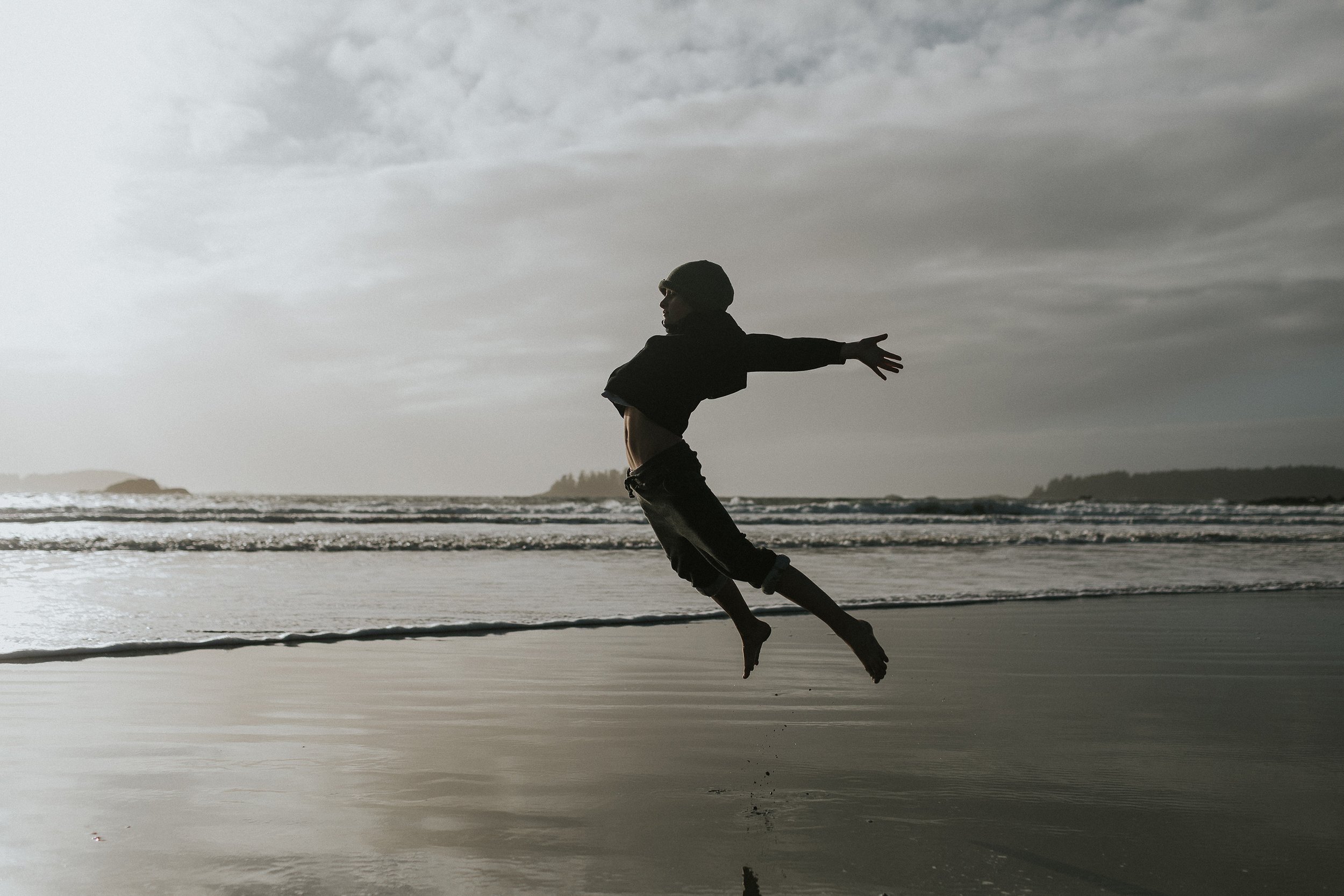 A silhouette of a child joyfully leaping on a beach at sunset, their reflection visible on the wet sand.