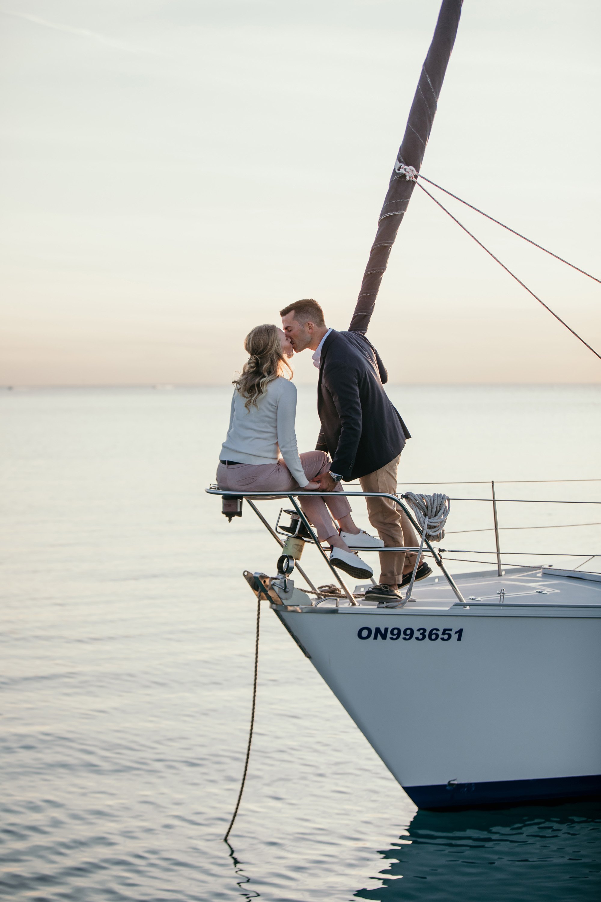 Couple sharing a kiss on the bow of a yacht at sunset, capturing a romantic moment on the water in Ontario.