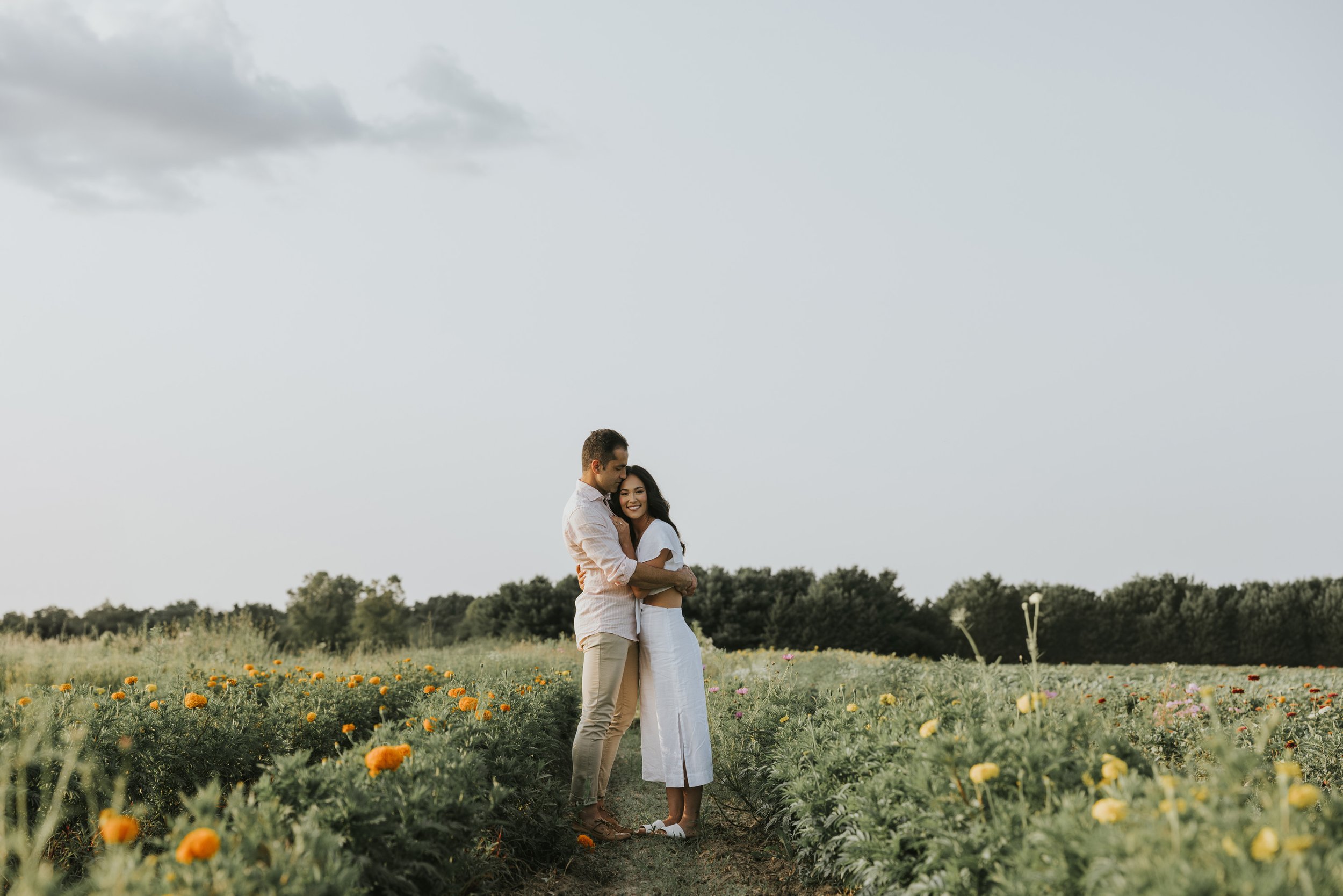 A couple embracing in a field of wildflowers, surrounded by the soft light and natural beauty of a summer evening.