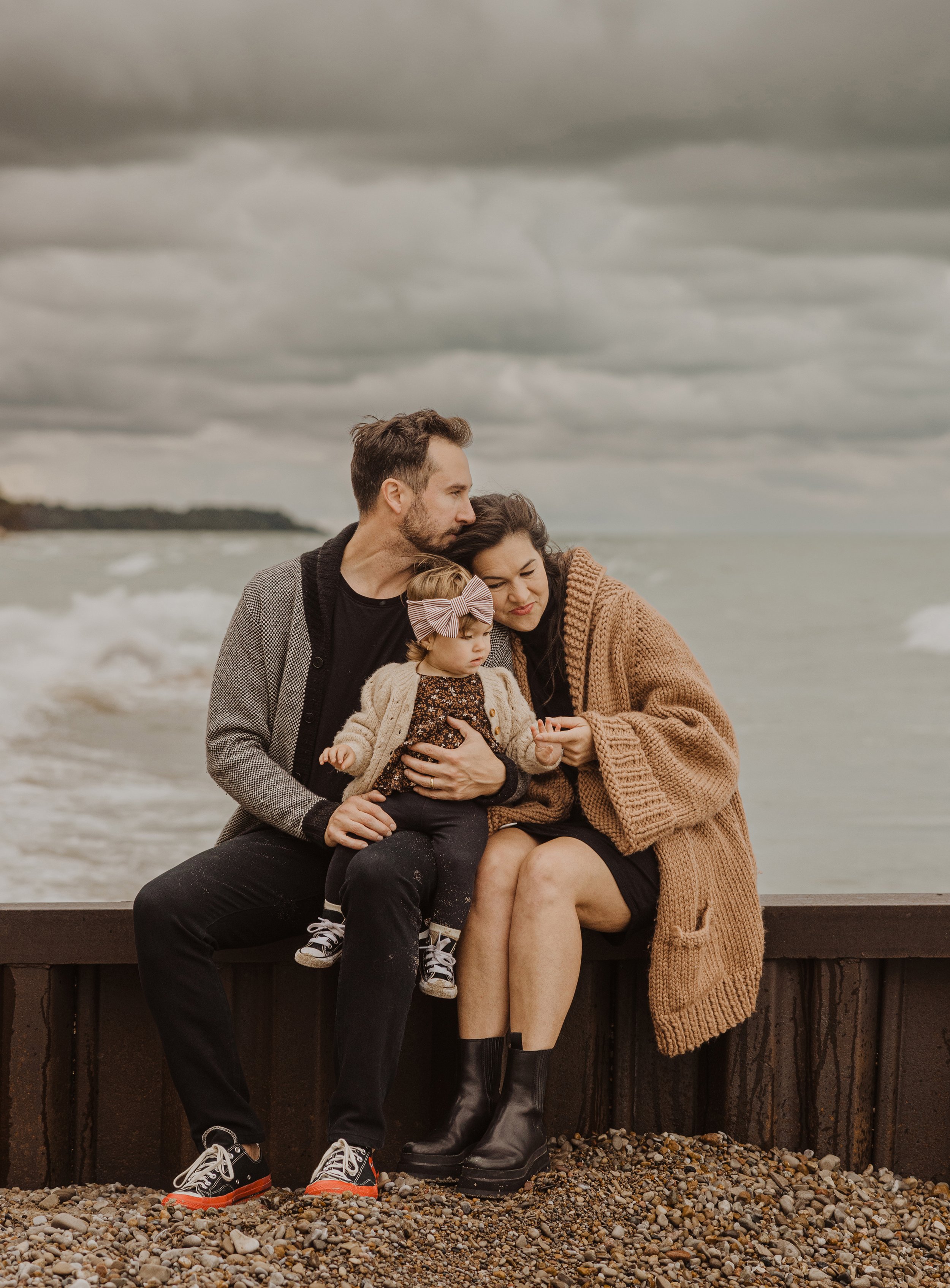 A candid moment of a family sitting together on a beach, with stormy skies overhead, capturing their connection and warmth despite the moody weather.