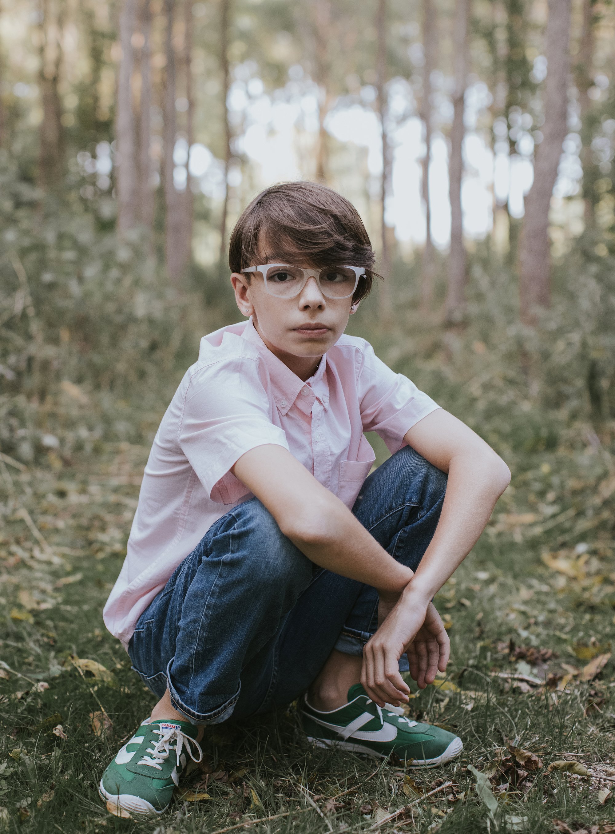 Teen Boy Portrait Forest London Ontario Photography: A portrait of a teen boy with glasses, sitting in a forest, wearing a pink shirt and jeans.