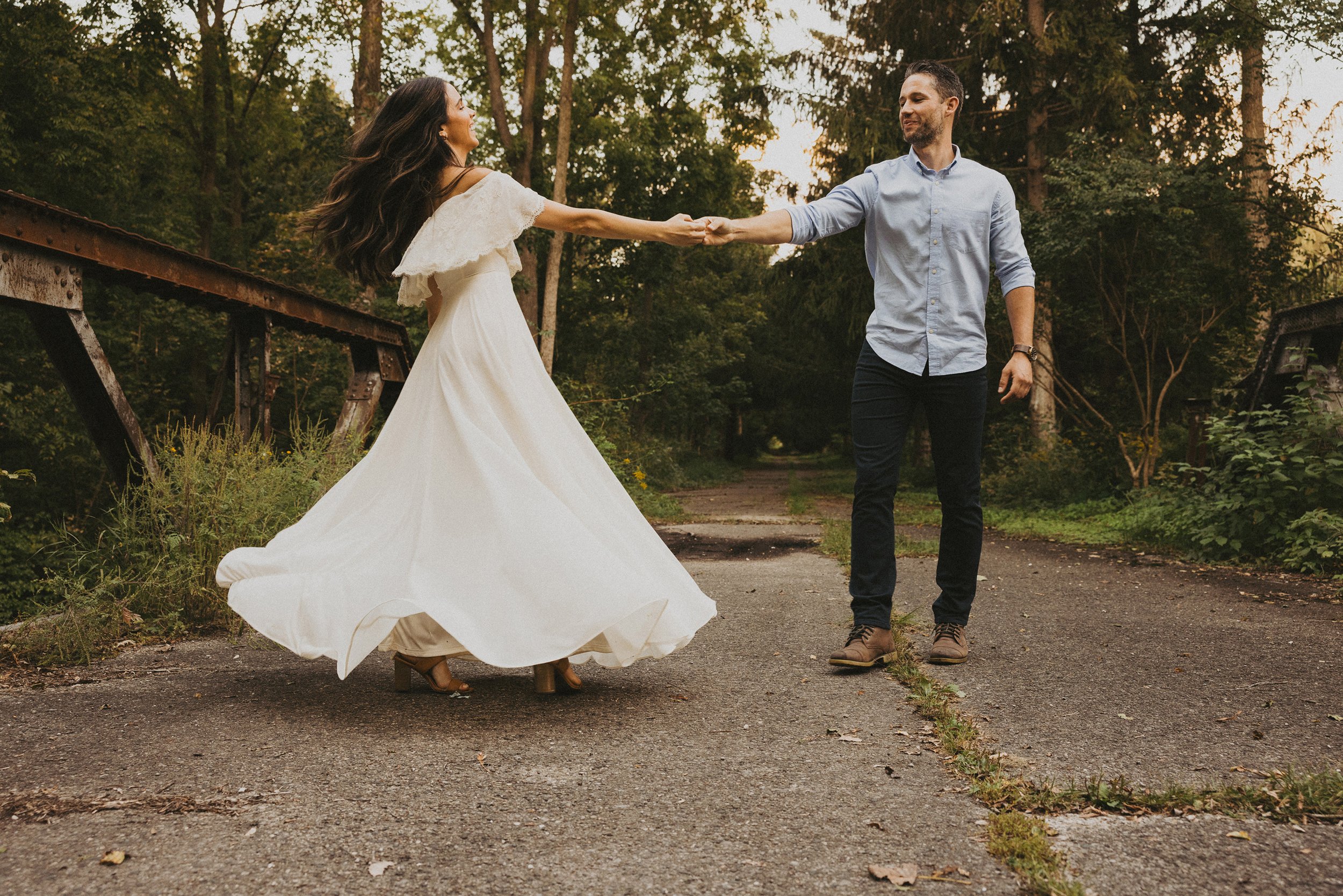 A couple shares a romantic dance on a forest path, with the movement of the dance captured beautifully against the backdrop of lush greenery.