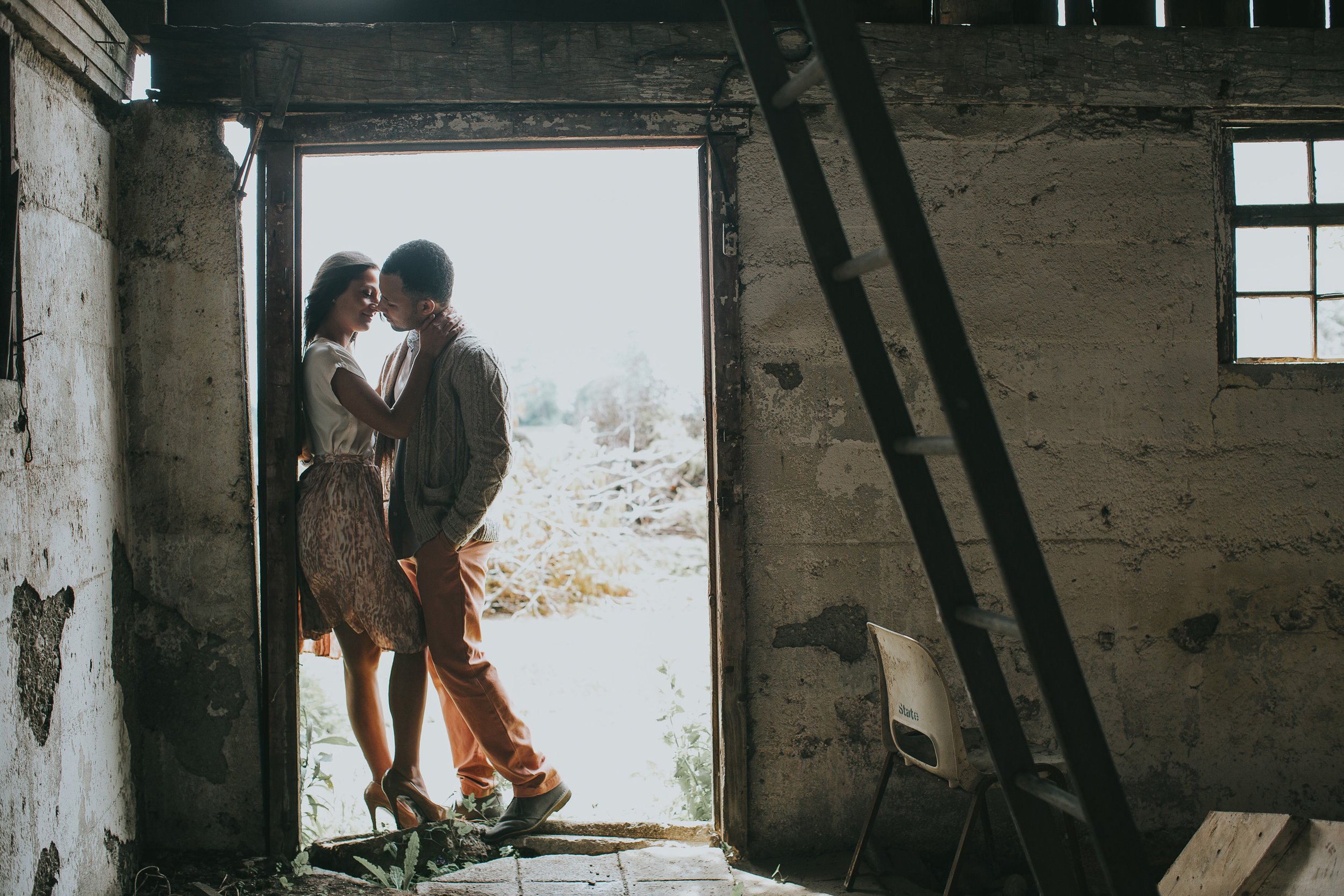 A couple shares a loving embrace in the doorway of an old barn during their engagement session. The rustic setting adds a charming, nostalgic feel to their connection.