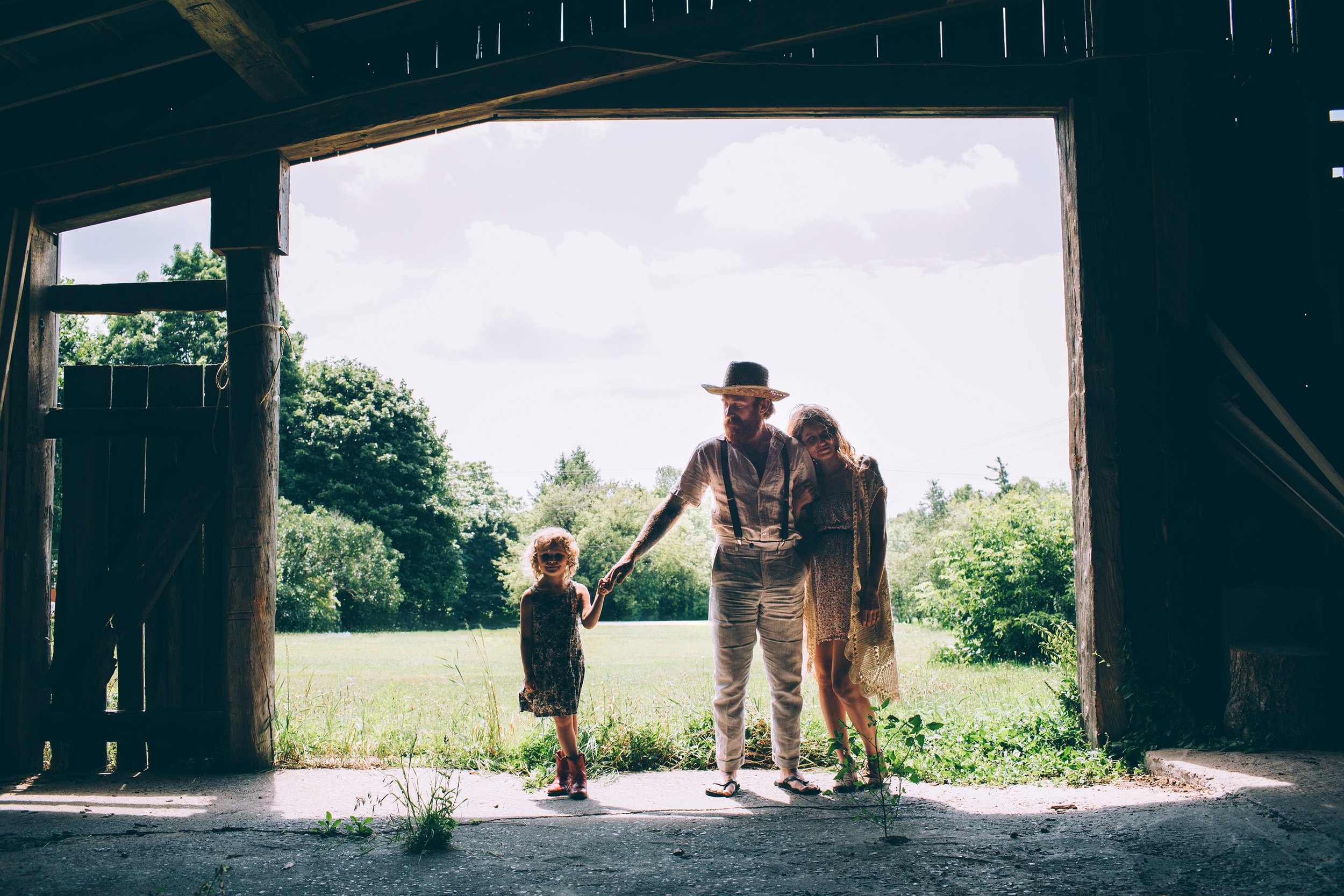 A family standing in the entrance of a barn, backlit by the warm sunset, capturing a rustic and serene moment.