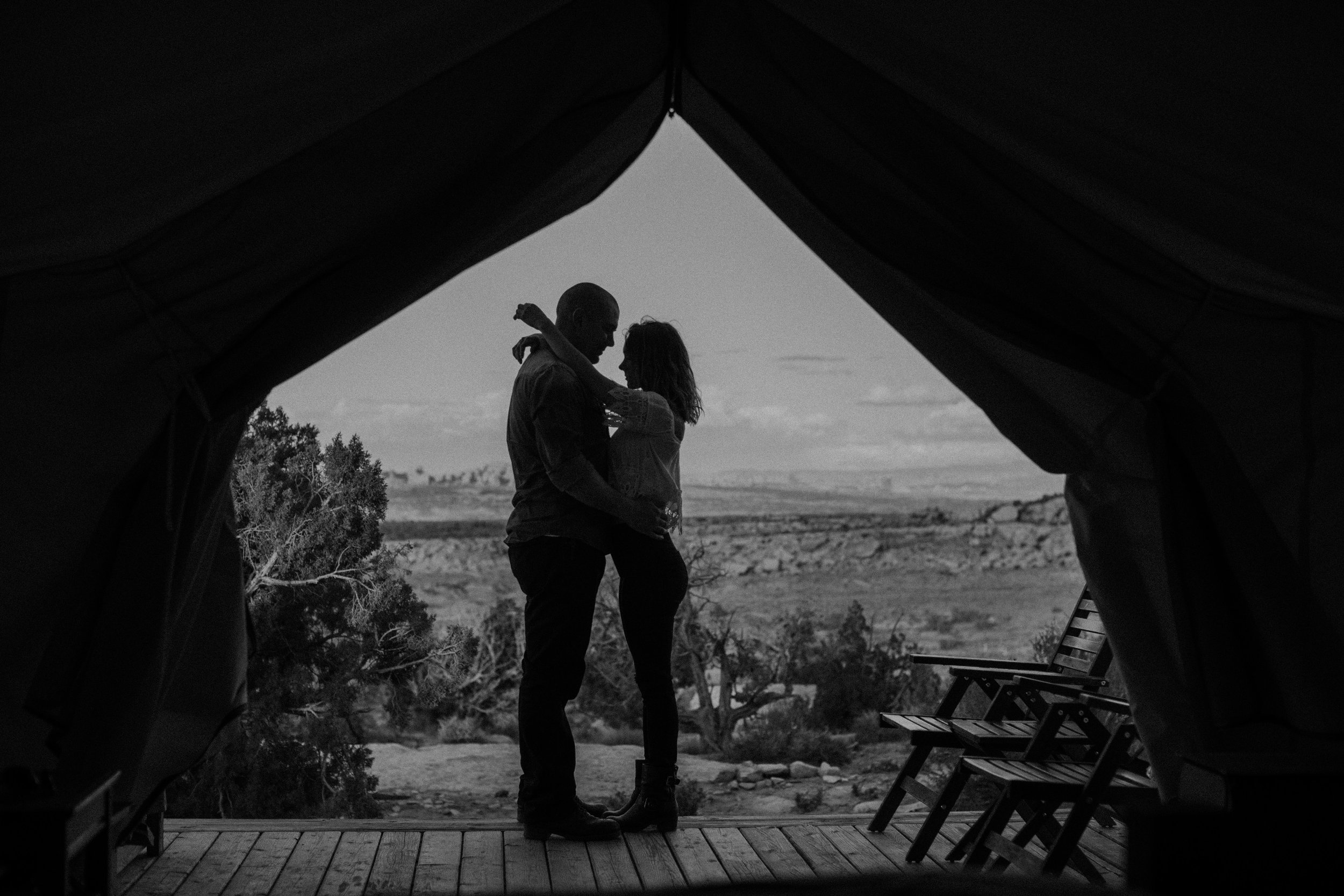 Silhouette of a couple embracing in the entrance of a tent, with an expansive desert landscape in the background.