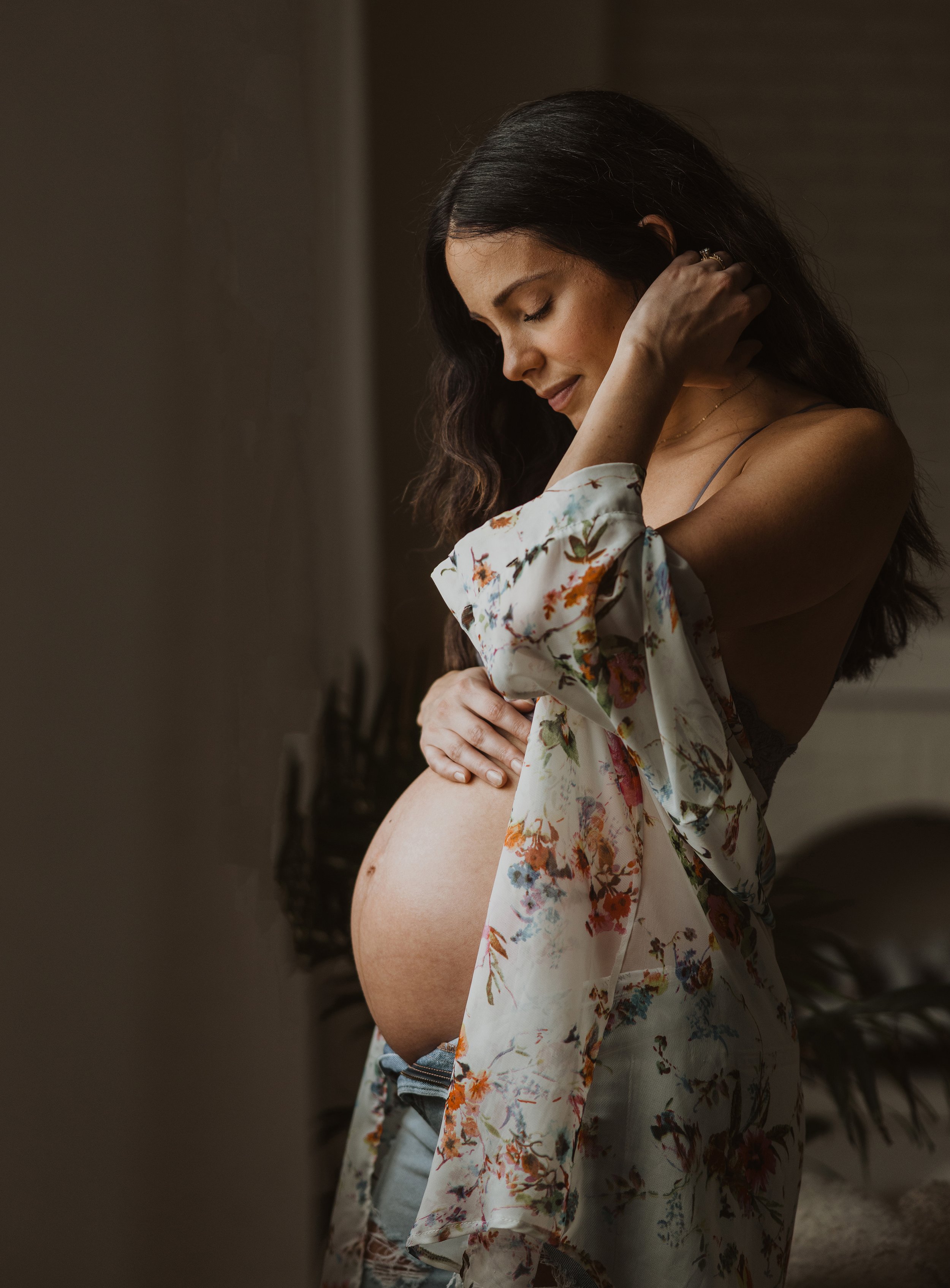 A pregnant woman softly cradling her belly, bathed in natural light, with a calm and serene expression.