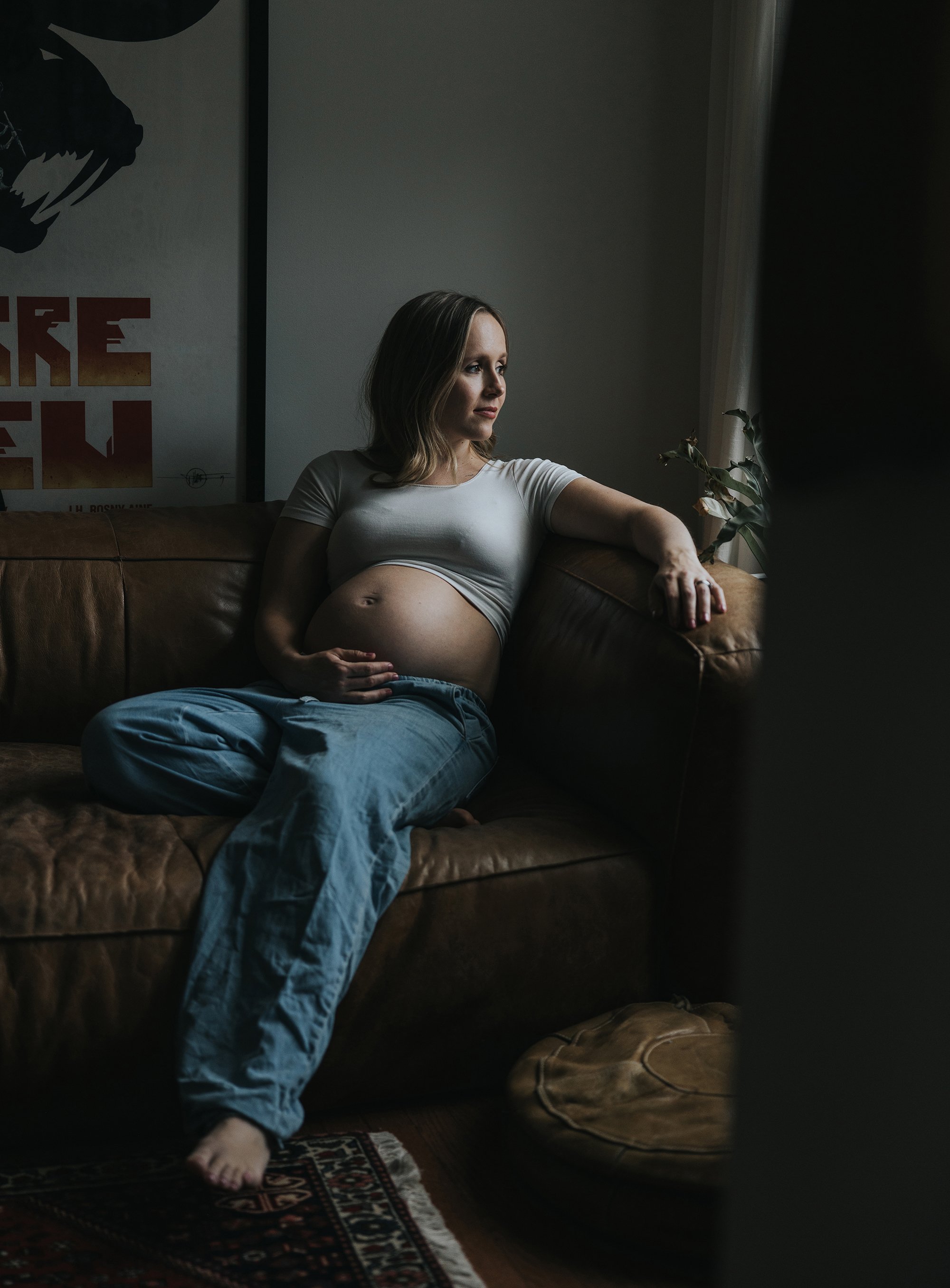 A serene maternity portrait featuring a woman gently holding her pregnant belly, standing in a softly lit room.