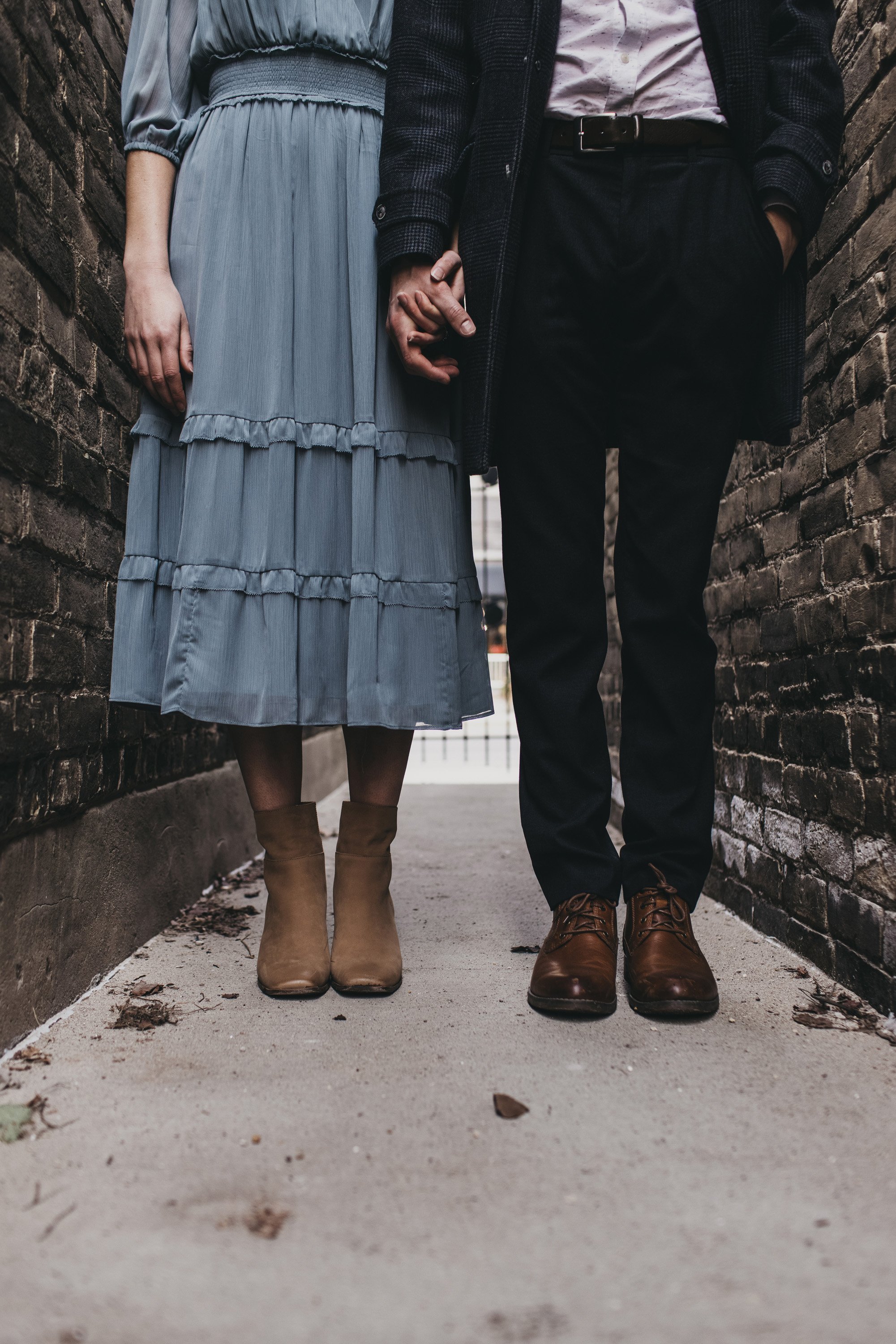 A close-up of a couple holding hands in a narrow alley, highlighting their vintage-inspired outfits.