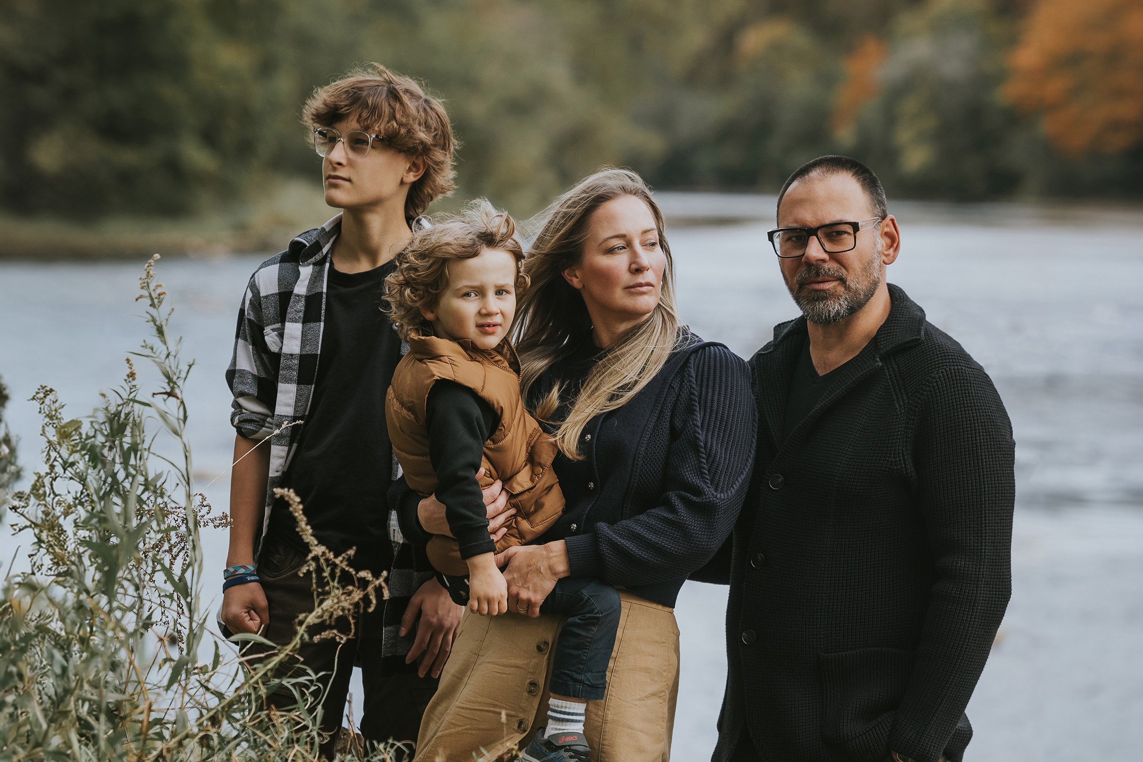 A family posing together by a river in the autumn, surrounded by the natural beauty of the season.