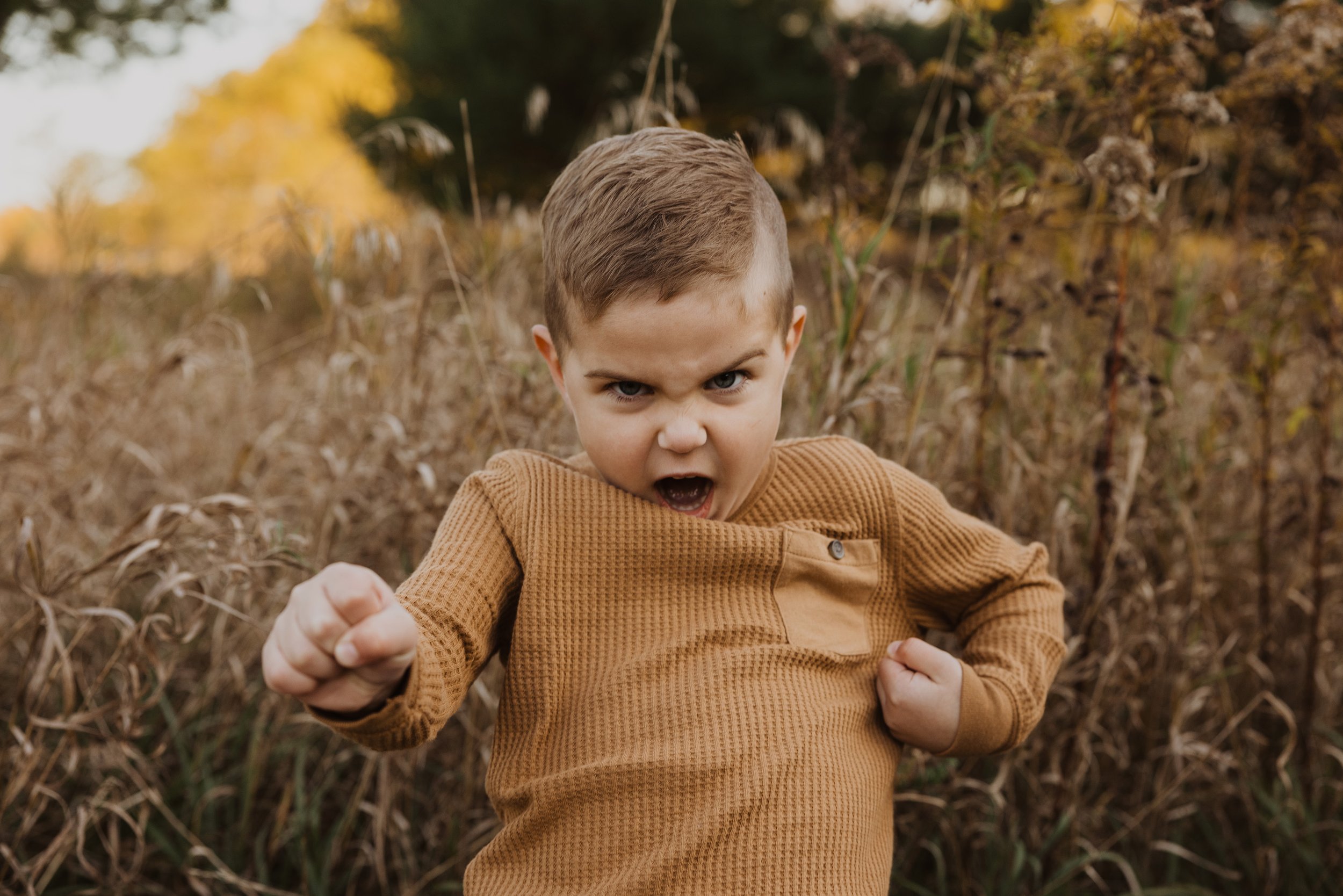 A young boy with an intense expression striking a pose in an autumn field, surrounded by tall grass.