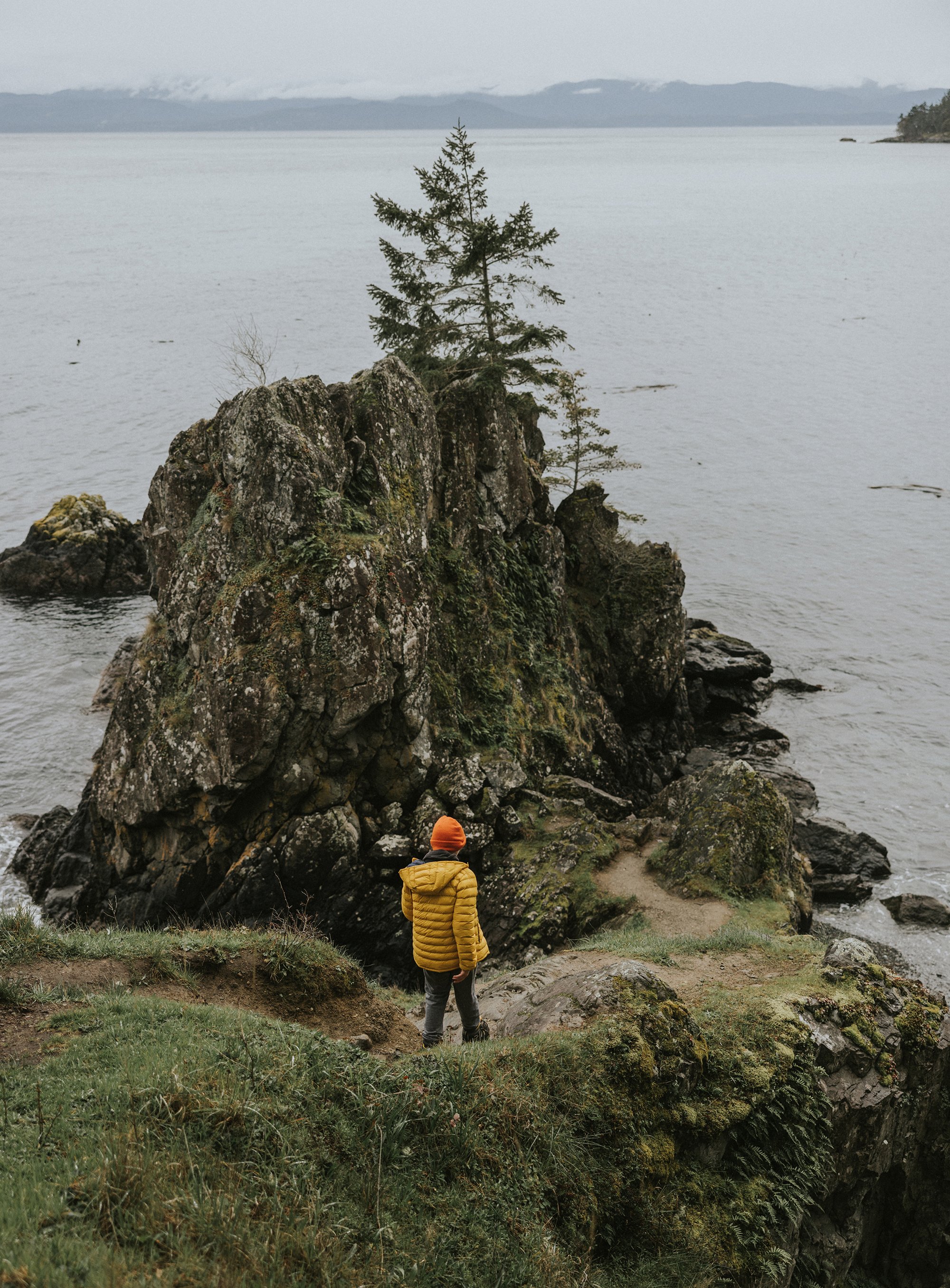 A child exploring the seaside cliffs in a bright puffer jacket, with a scenic coastal view in London, Ontario.