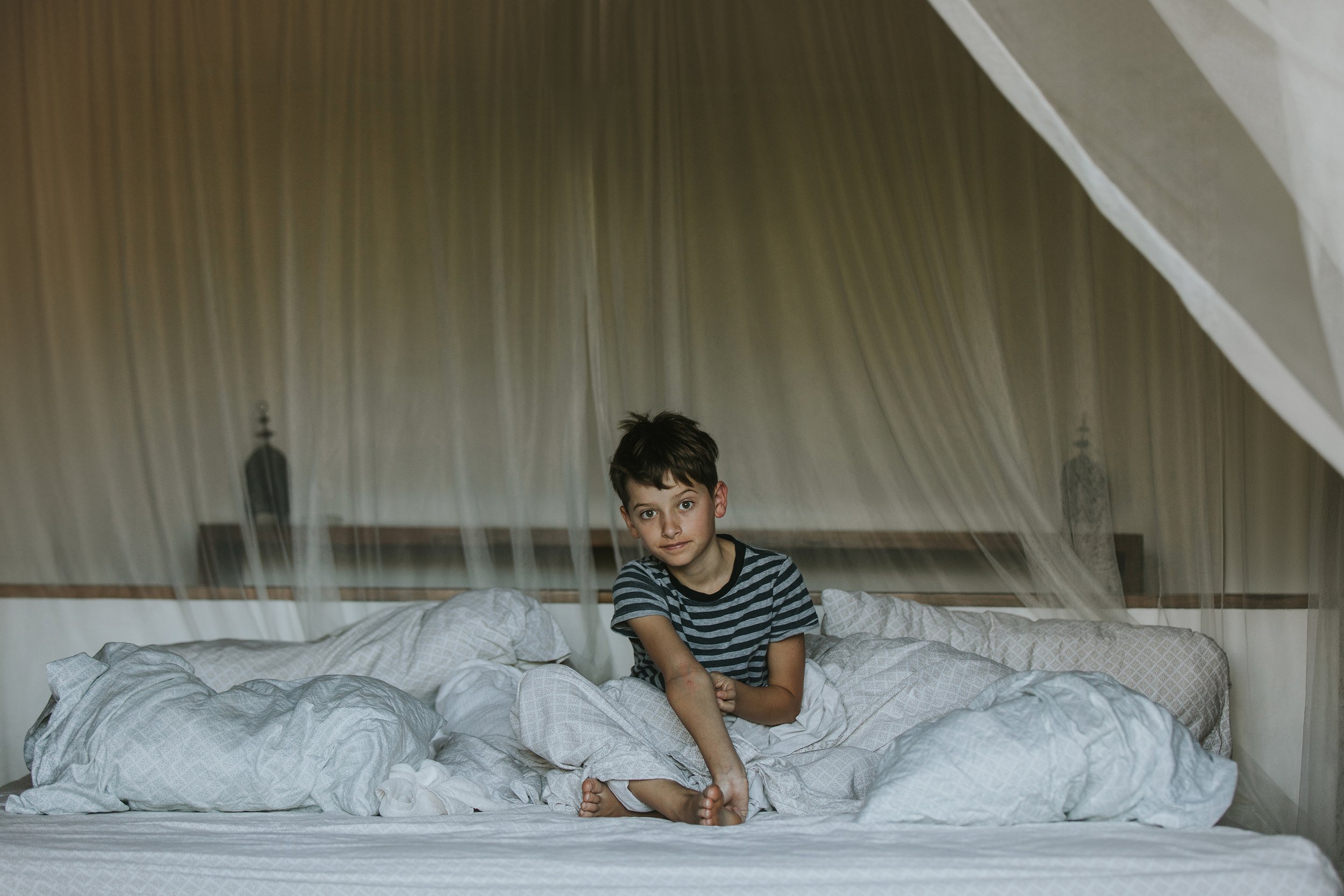 A candid morning portrait of a boy sitting on a bed, surrounded by cozy blankets, in London, Ontario.