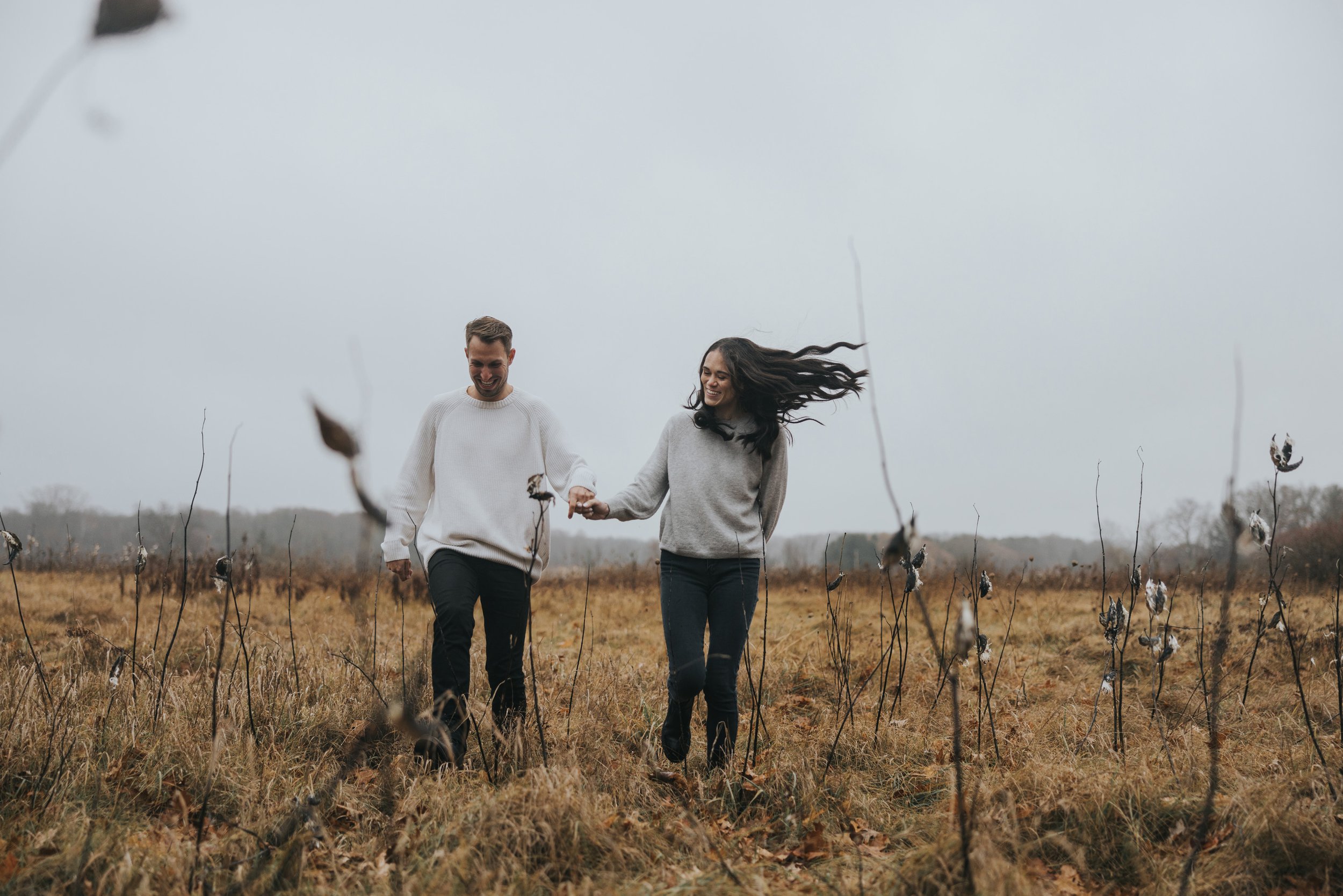 A couple walks hand in hand through an autumn meadow, the wind gently blowing their hair as they enjoy a peaceful moment together in nature.