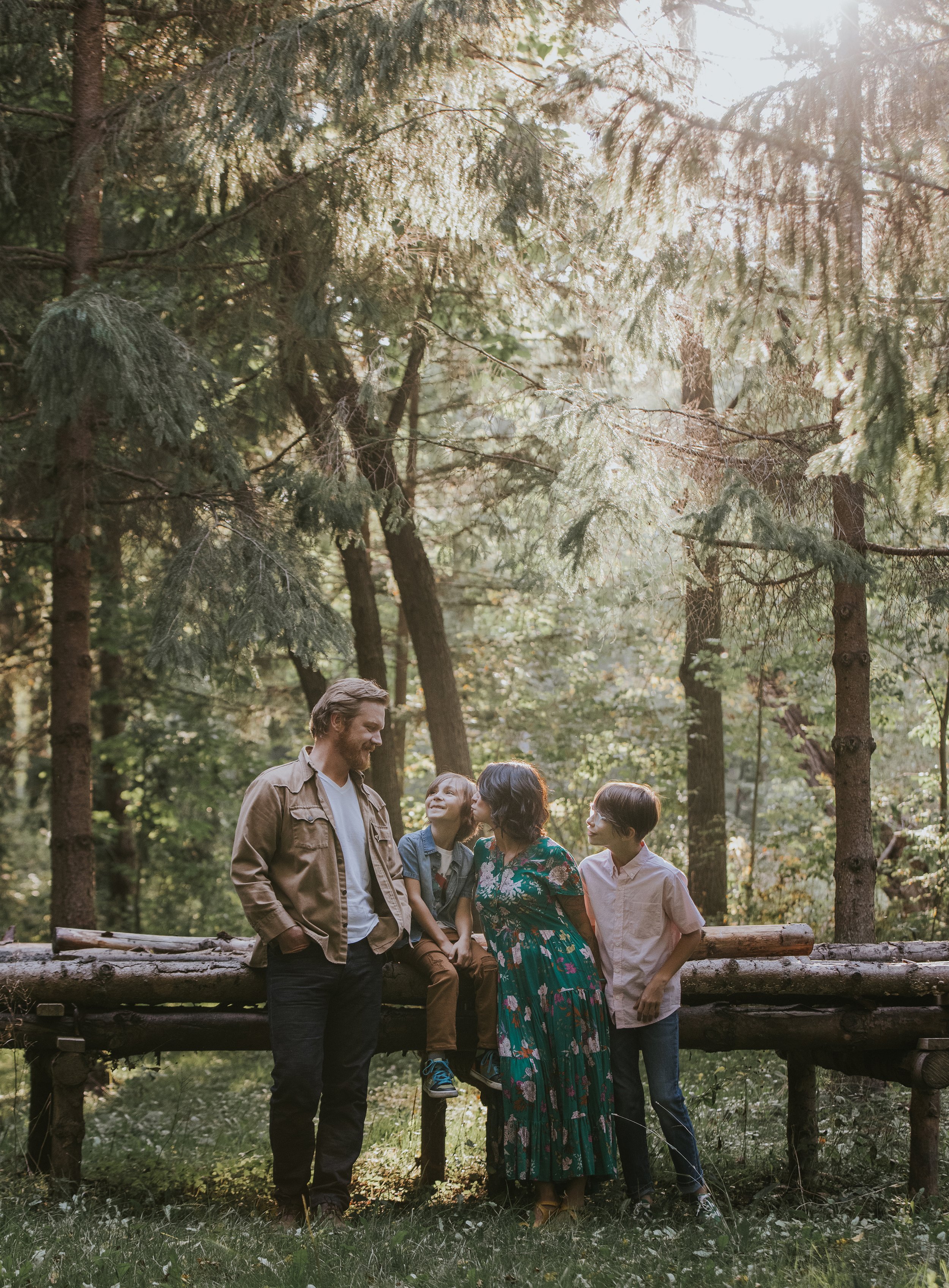 A family of four enjoying a warm moment together in a forest, bathed in the golden light of sunset, with tall trees surrounding them.