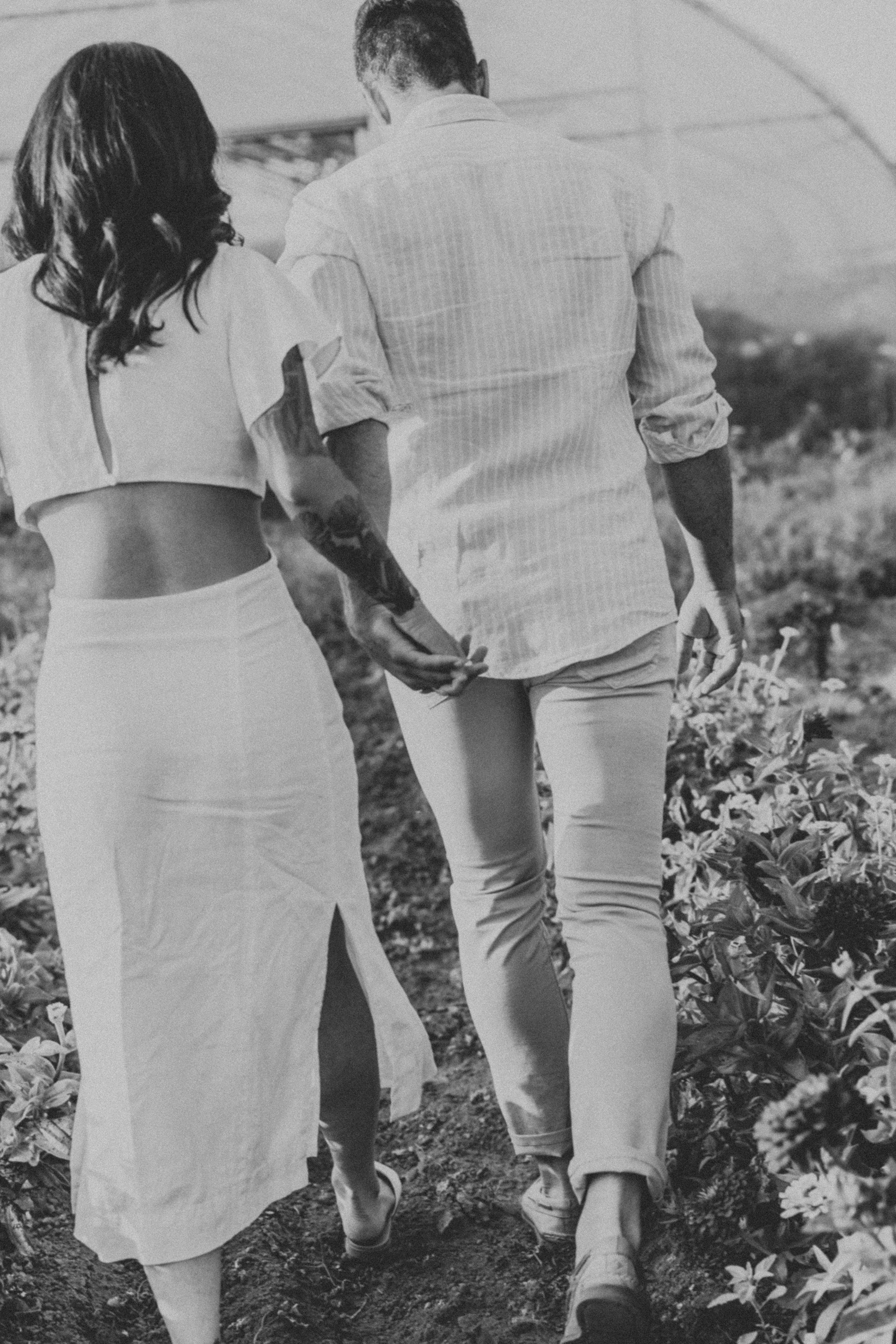 A black-and-white photograph of a couple holding hands as they walk through a field, capturing their connection and simplicity.