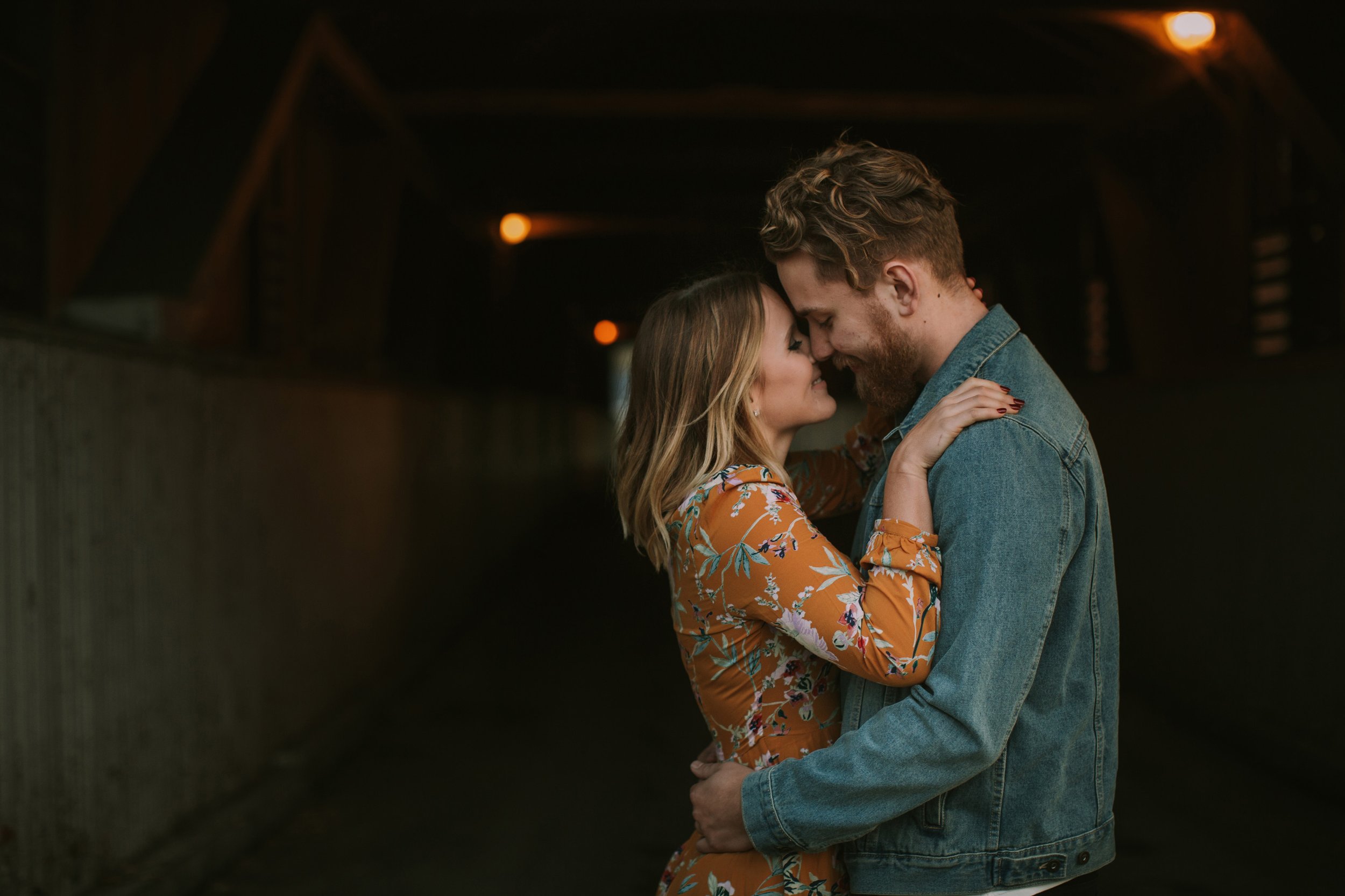 A couple shares a tender moment, embracing in a dimly lit tunnel during an engagement session, creating a warm and intimate atmosphere.
