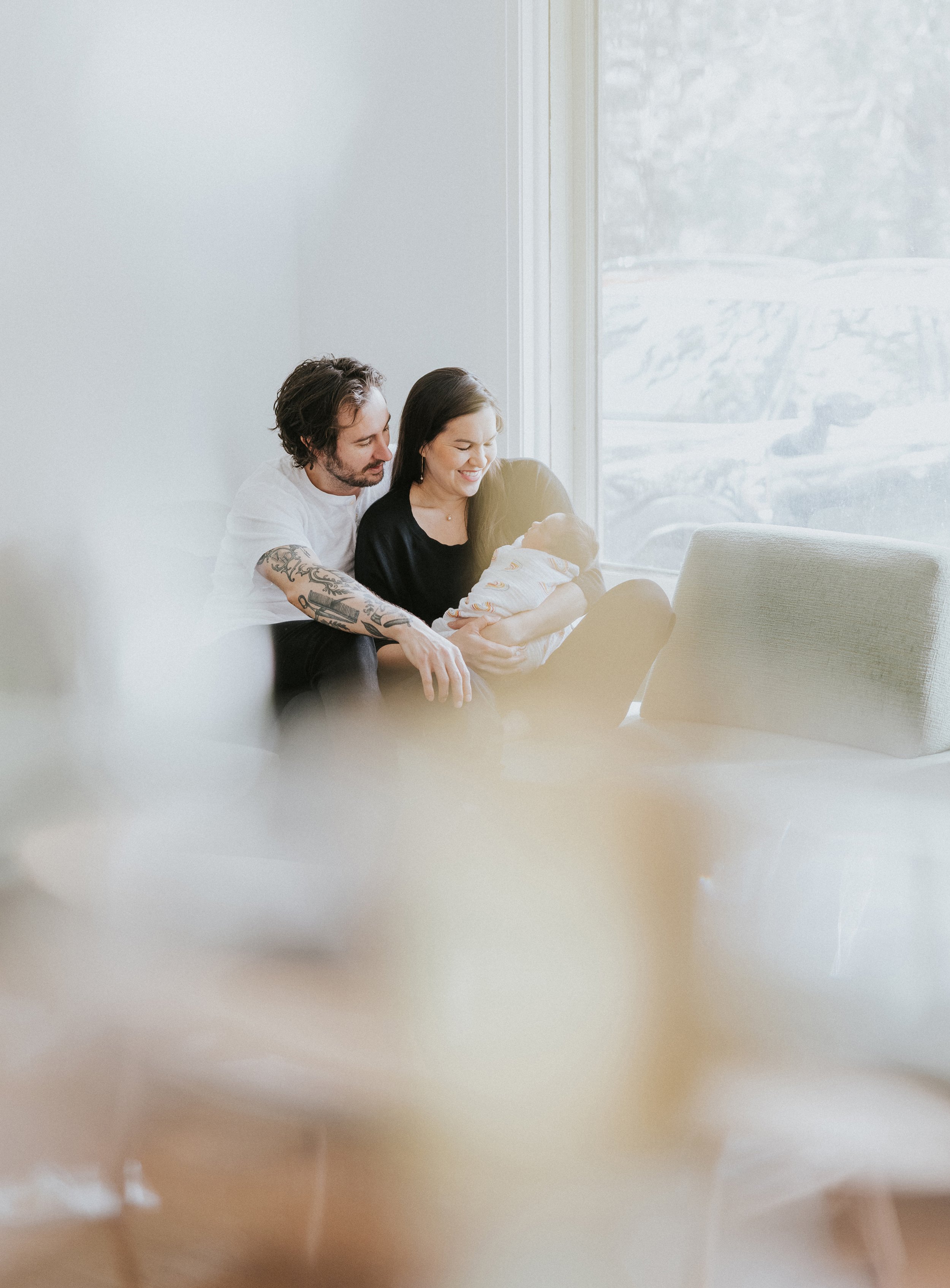 Parents holding their newborn baby with soft, diffused light pouring through a nearby window, creating a dreamy, intimate atmosphere.