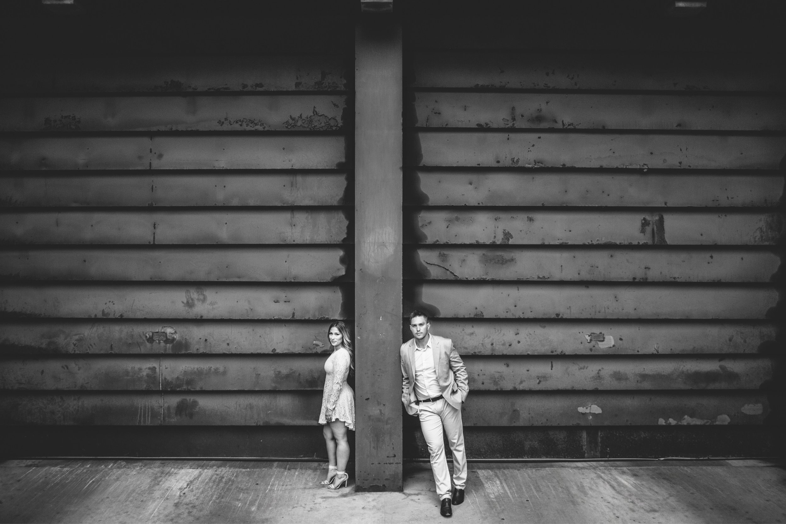 A couple posing against an industrial urban backdrop, capturing a modern engagement scene.
