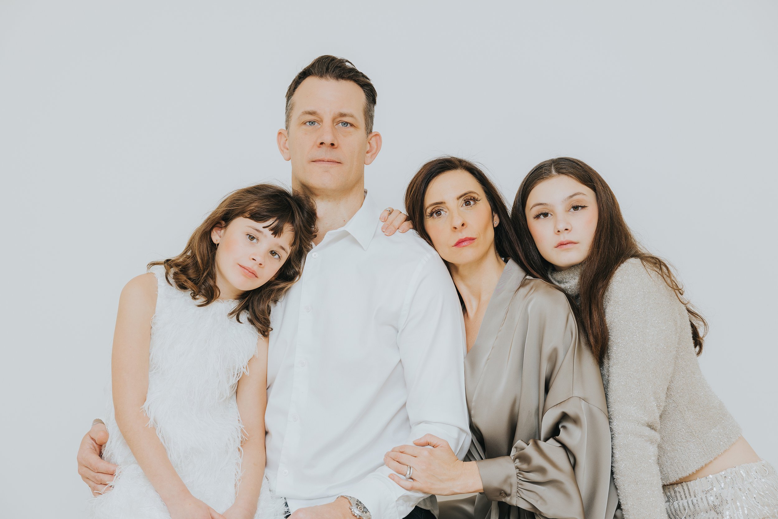 A modern family portrait with neutral tones, featuring parents and children posing closely together.