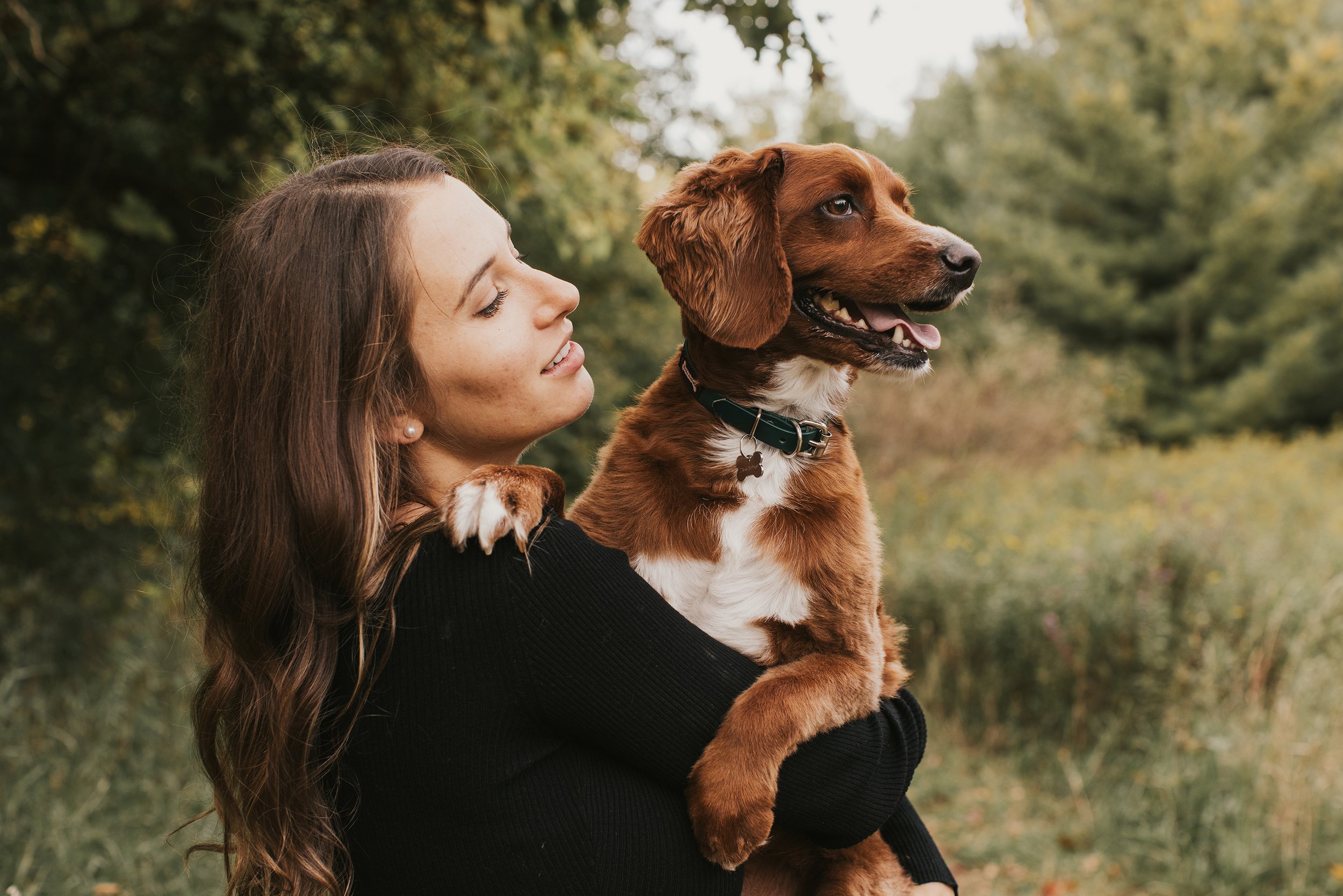 A woman hugging her dog during a maternity photoshoot in a peaceful outdoor setting.