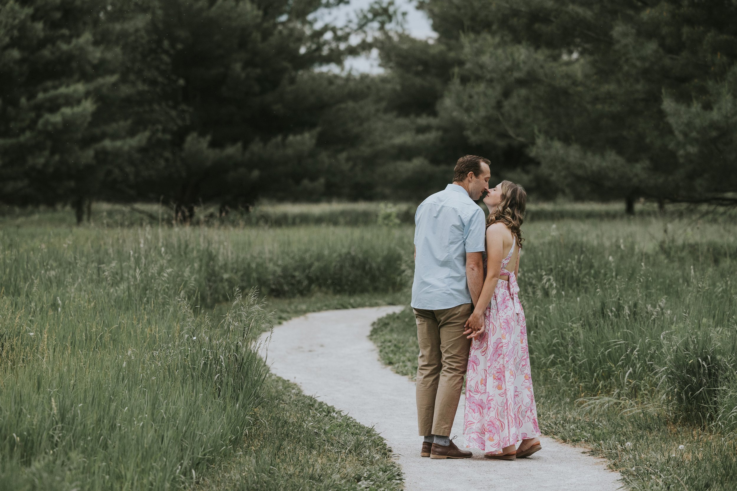 A couple shares a kiss on a scenic pathway surrounded by lush greenery.