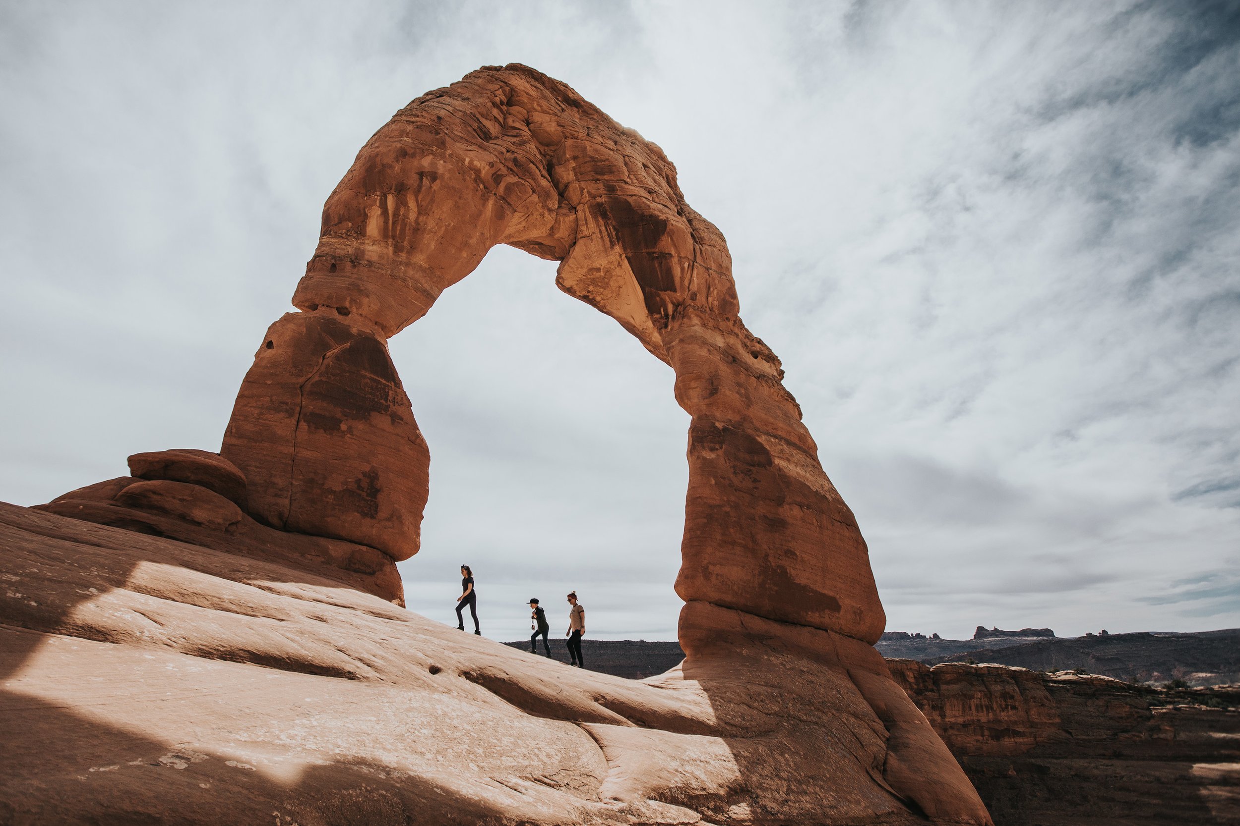 A family hiking near Delicate Arch, with the towering natural rock formation framing them against a vast, open sky.