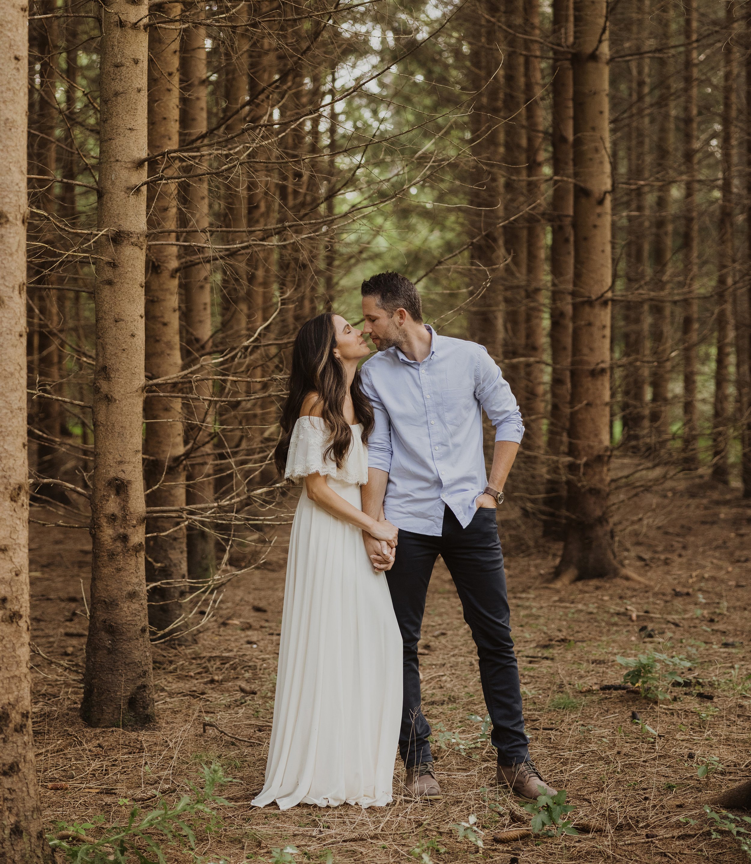 A couple sharing a romantic kiss in a forest during their engagement session in London, Ontario.