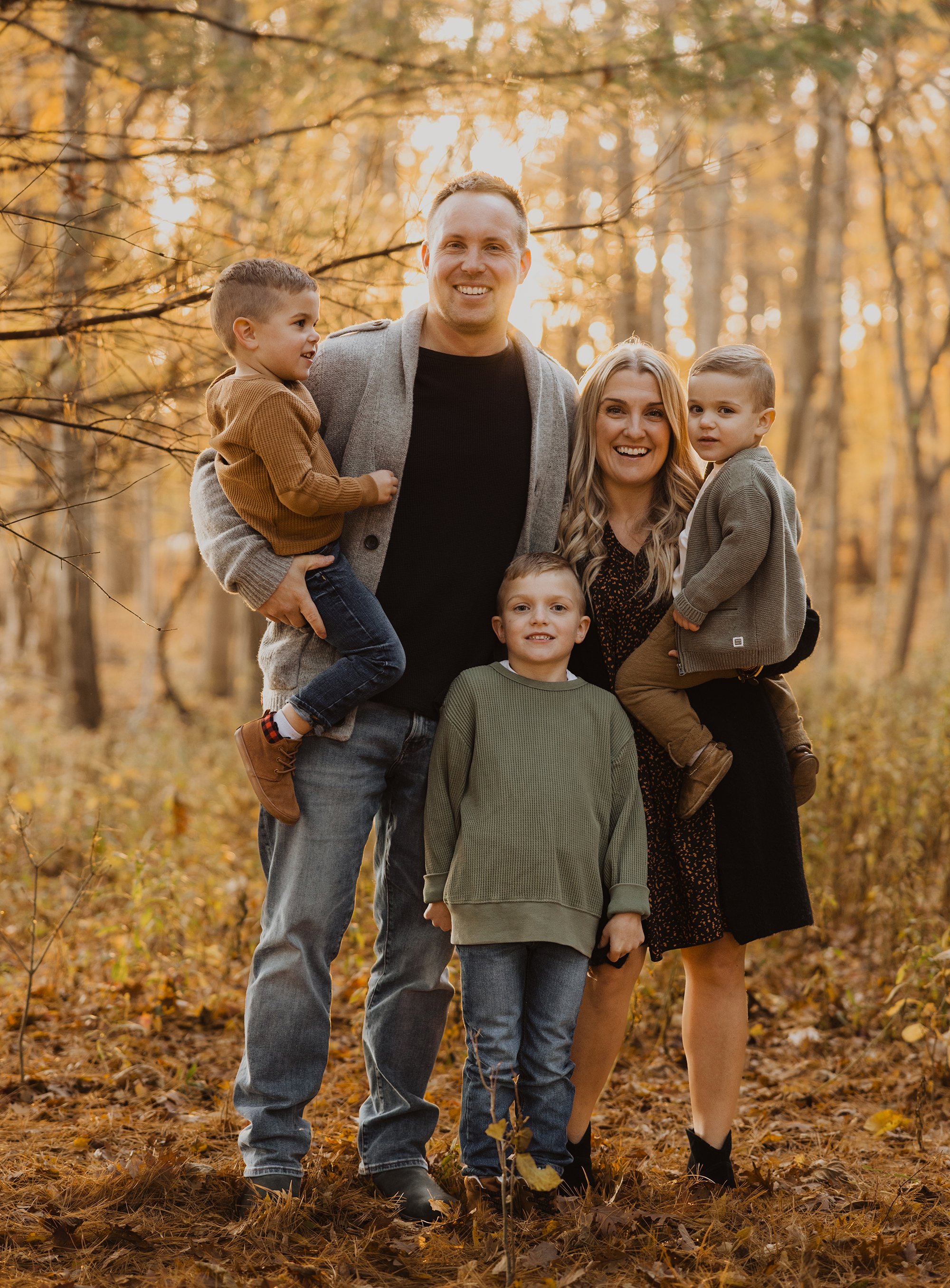 A cheerful family portrait taken in a fall forest, with sunlight filtering through the trees, creating a warm, golden backdrop.