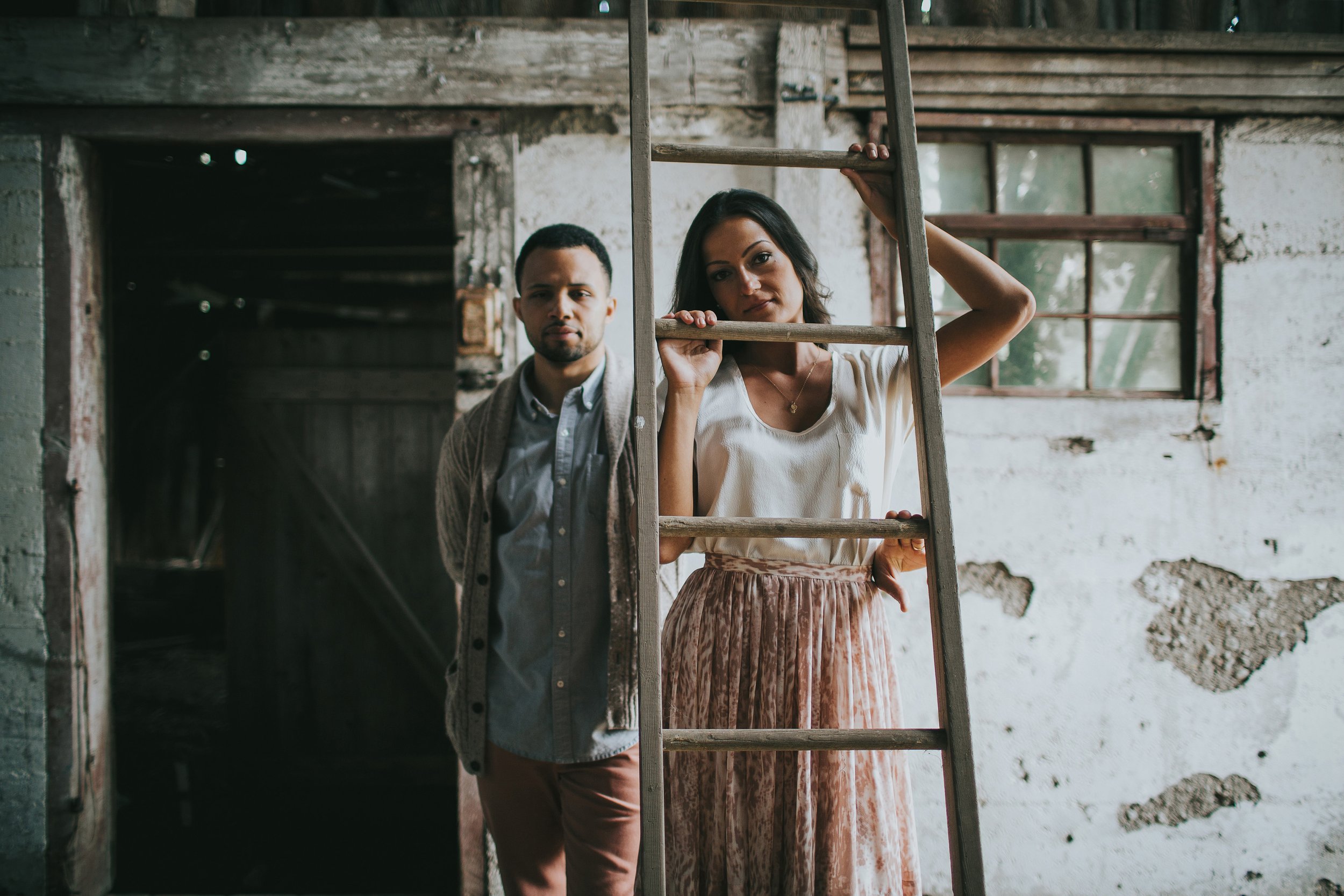 A couple poses with a rustic ladder in an old barn, capturing a vintage and nostalgic vibe in their engagement photo.
