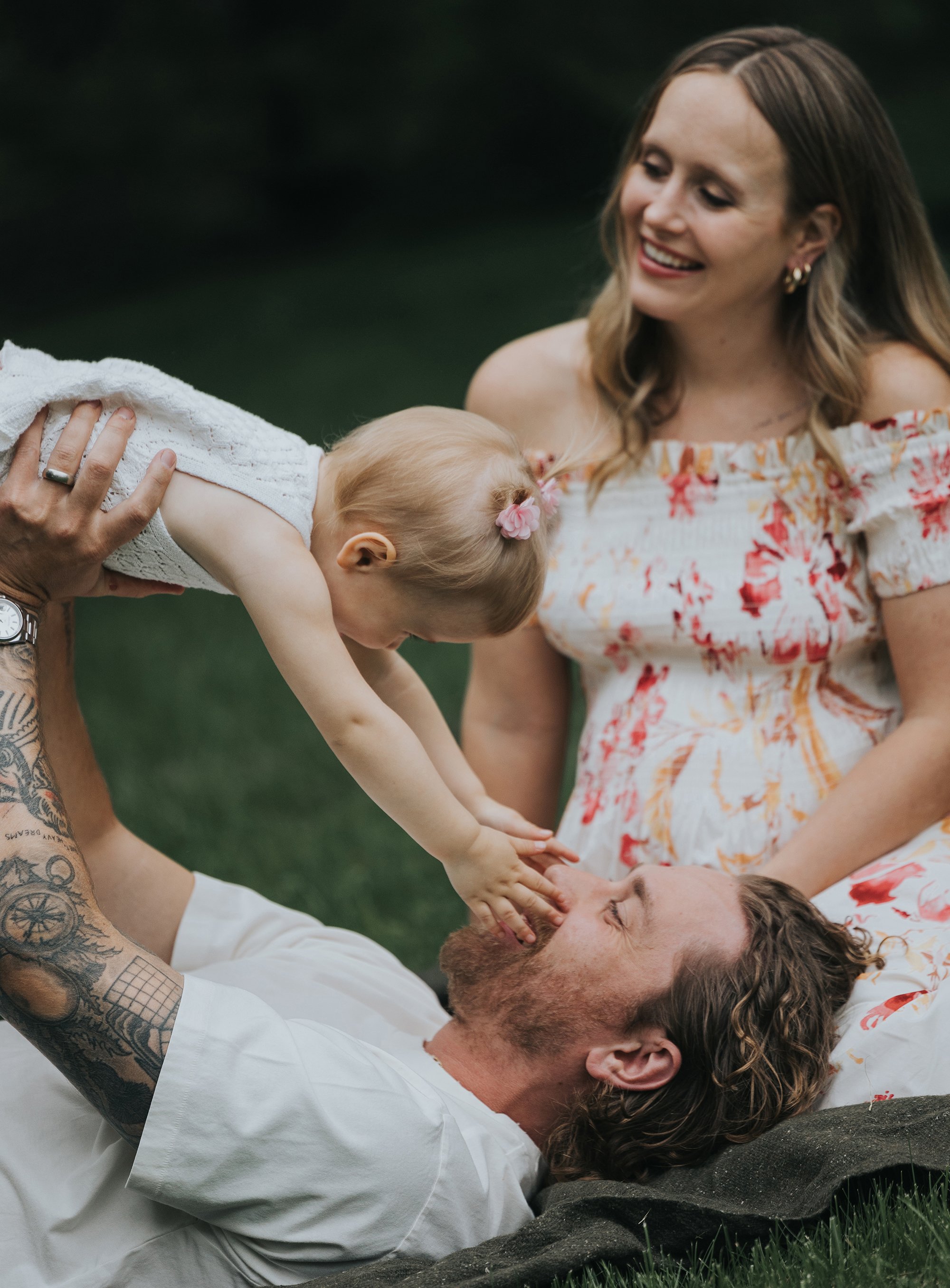 A candid outdoor family photo showing a joyful moment of cuddles and connection while lying on the grass in a relaxed setting.