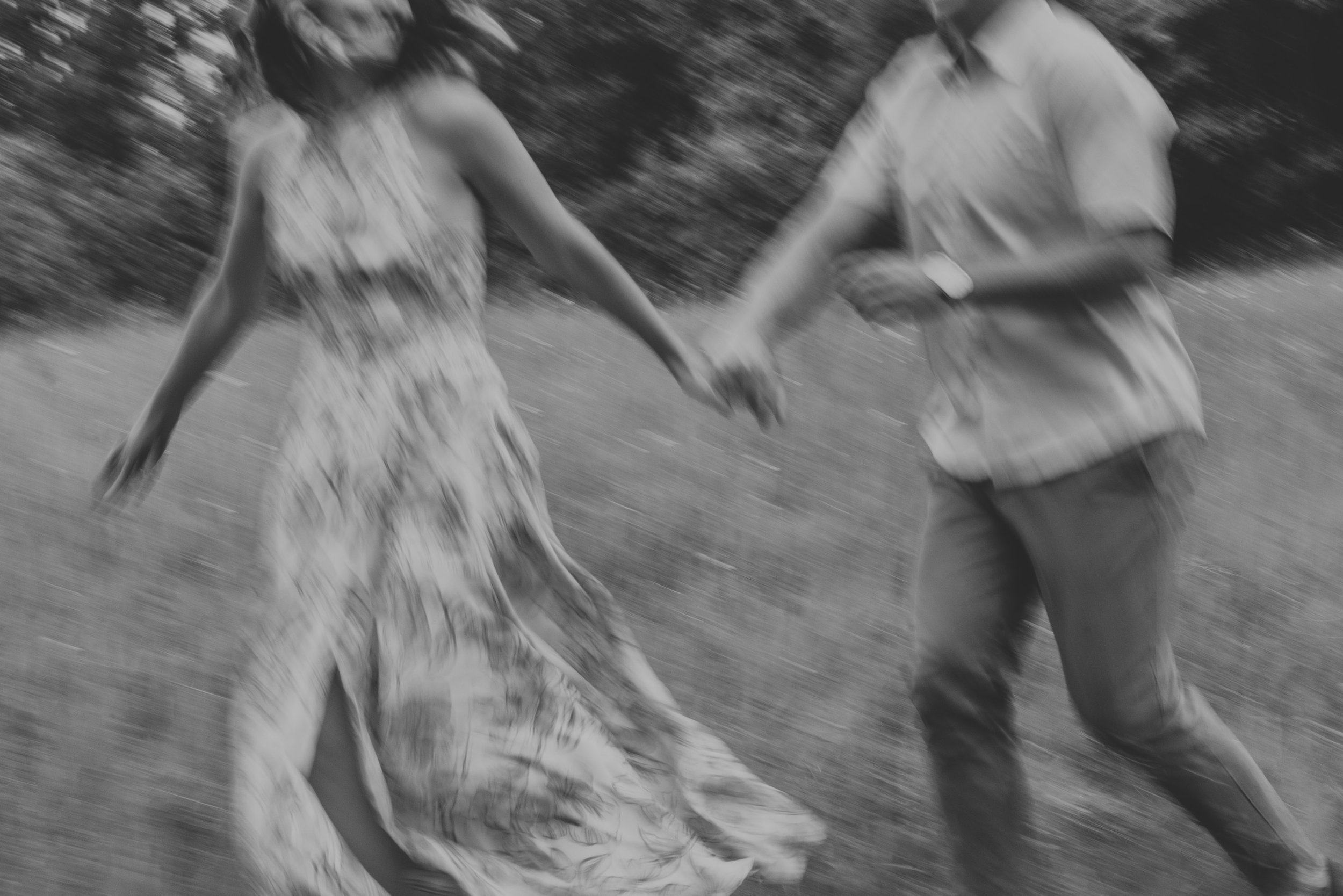 A blurred motion shot of a couple running hand in hand through a field, conveying a sense of joy and freedom as they share a playful moment.