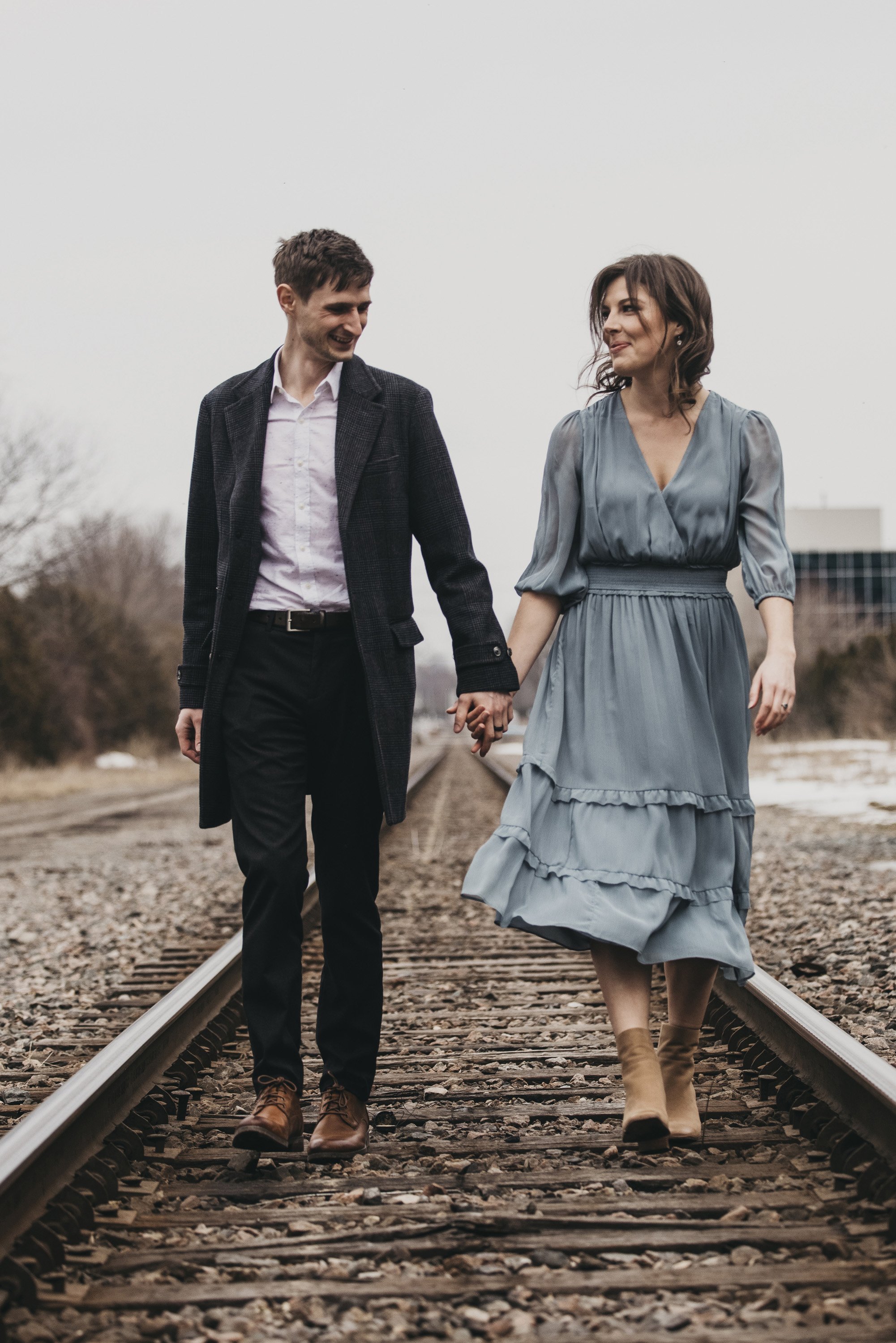A couple walking hand in hand along a railway track during their engagement session in London, Ontario.