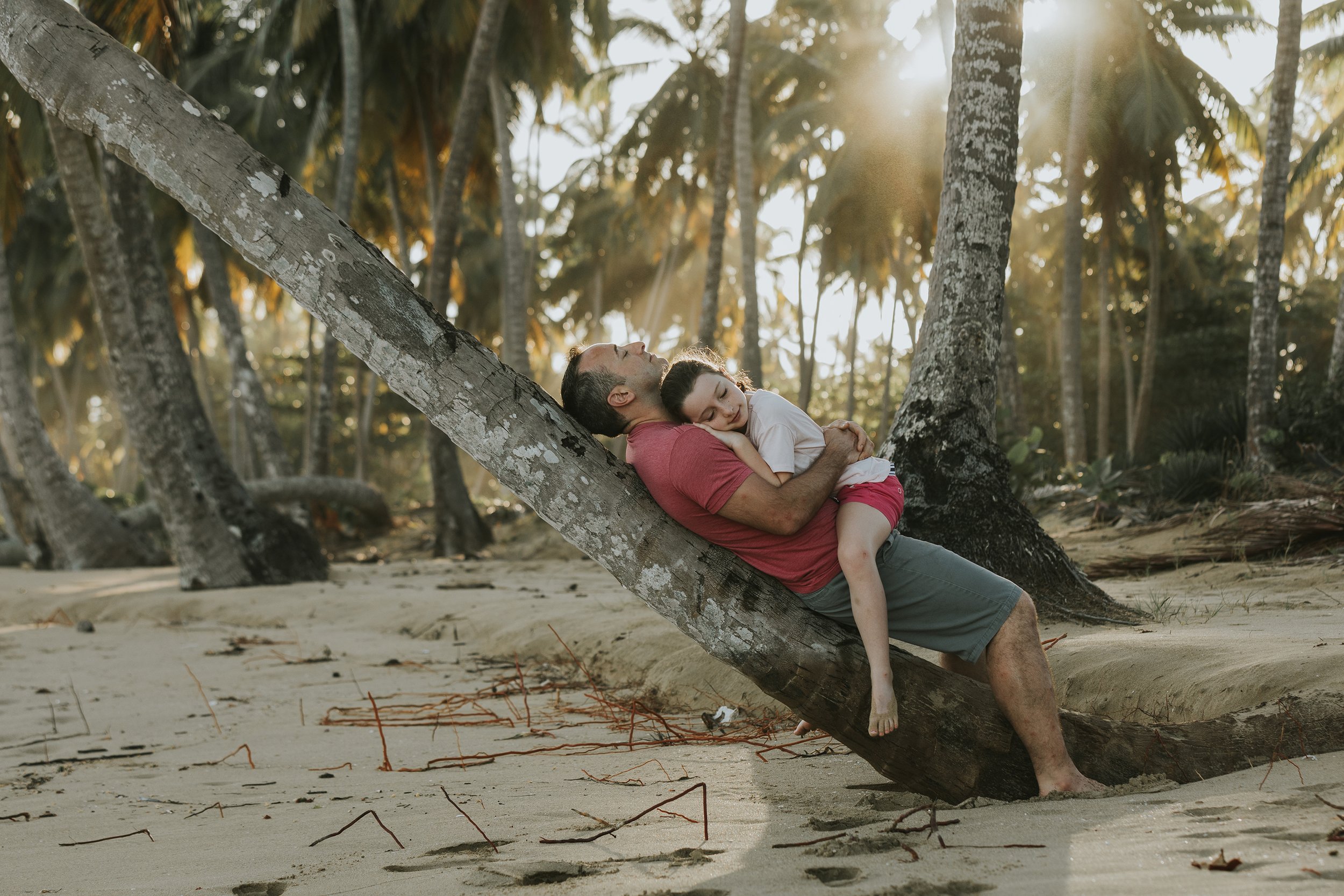 A father and daughter relaxing on a beach in London, Ontario, leaning against a palm tree and enjoying a serene moment together.