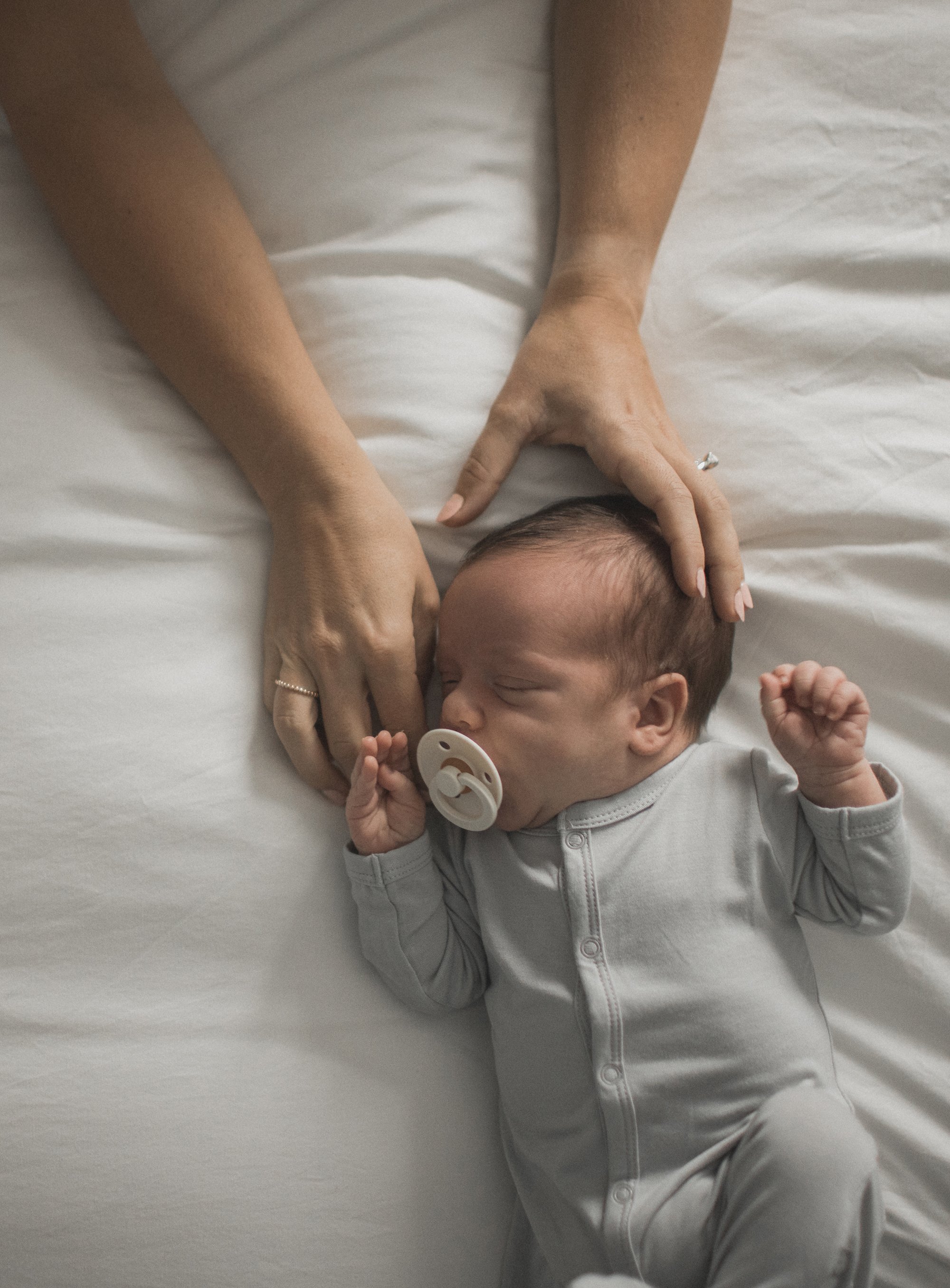 A close-up of a sleeping newborn with a pacifier, nestled beside their mother’s hands.