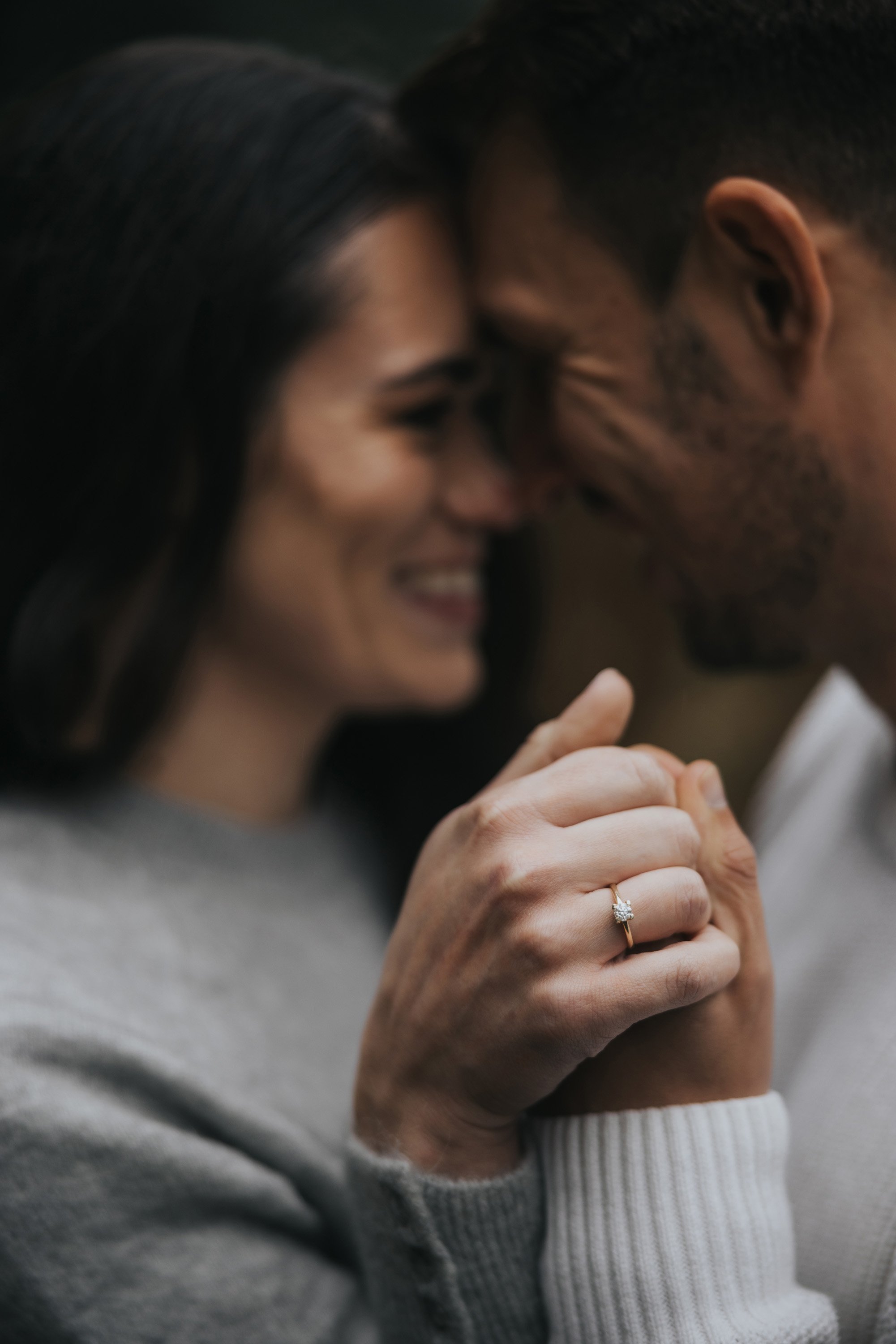 Close-up shot of a couple holding hands, with a focus on the engagement ring, highlighting the commitment and joy of their engagement.