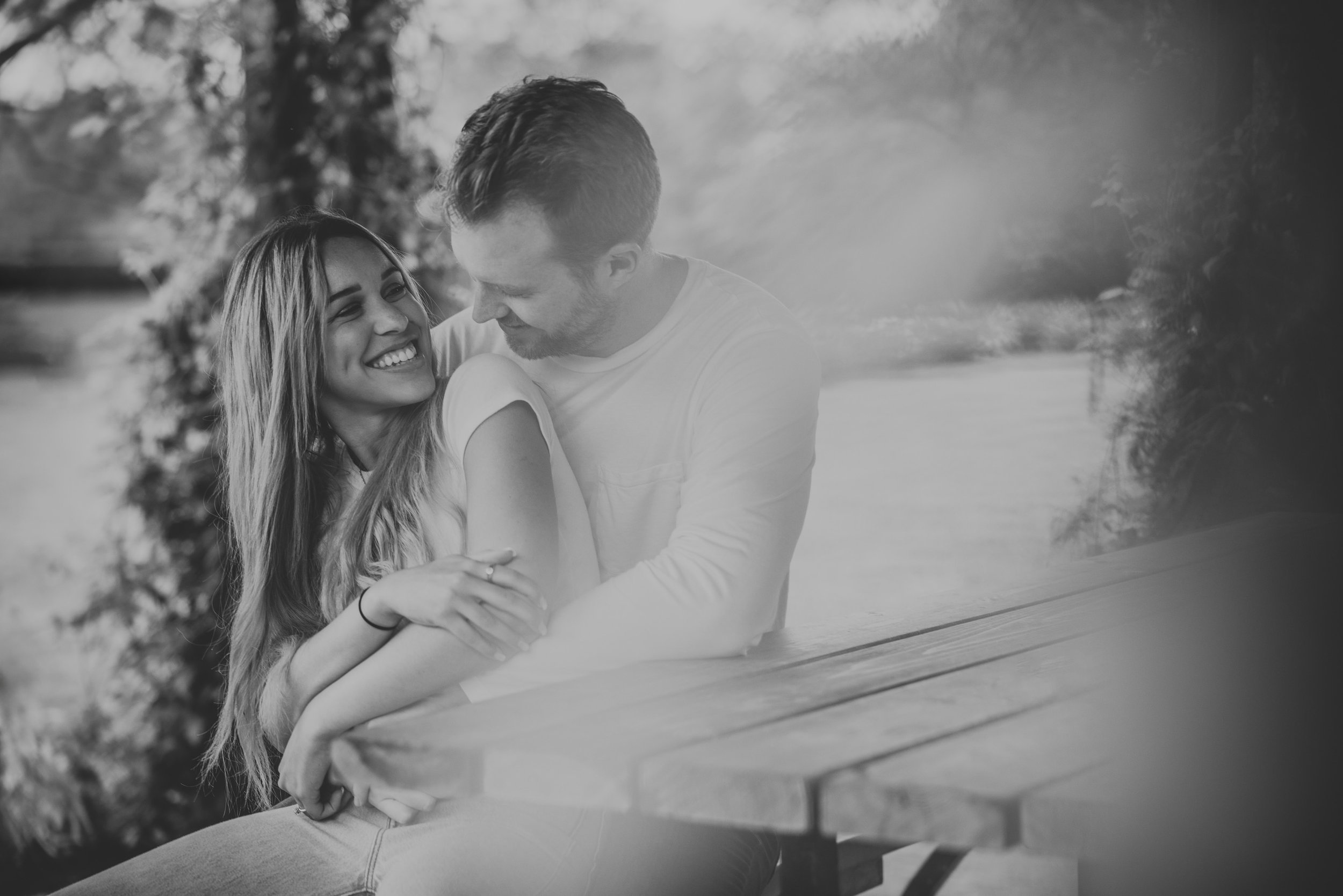 A romantic engagement photo of a couple standing in a shallow creek, embracing and surrounded by lush greenery, with the woman in a red dress and the man in a white shirt.