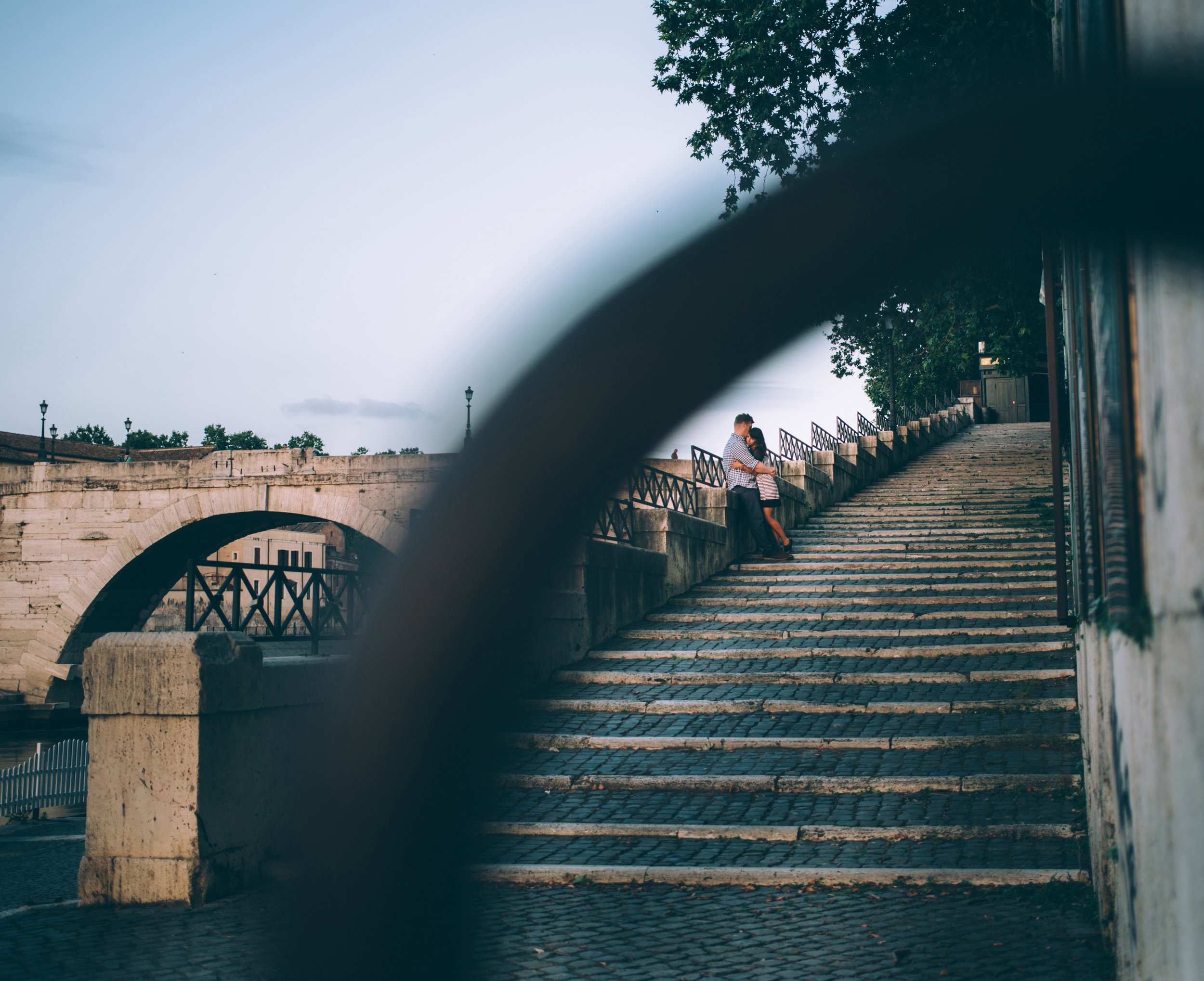 A couple shares a romantic moment on stone stairs in an urban setting, with soft light highlighting their embrace.