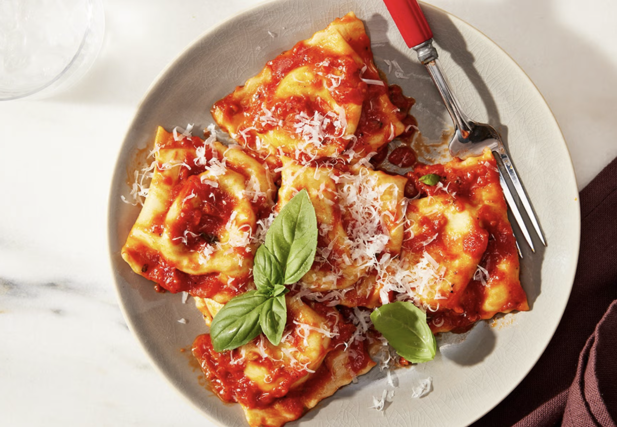 Plate of cheese ravioli with tomato sauce, grated cheese, and fresh basil leaves, with a fork on the side.