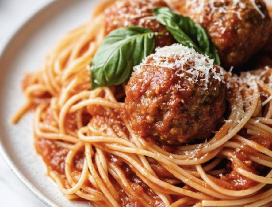 Spaghetti with meatballs garnished with basil and grated cheese.