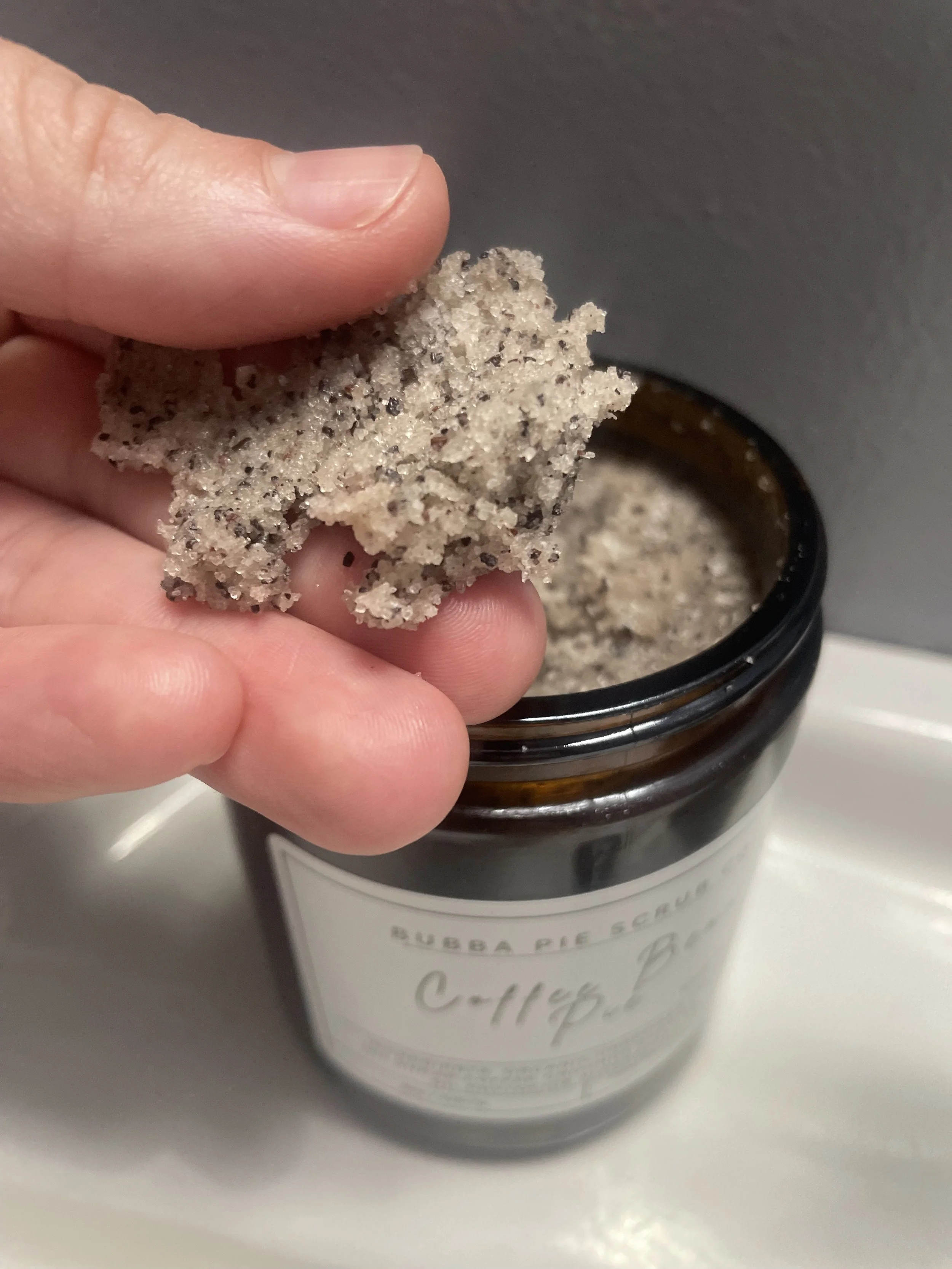 Person holding a speckled, possibly cookie or crumble-like snack over an open jar labeled 'Bubble Pie Scoop Coffee Bake'.