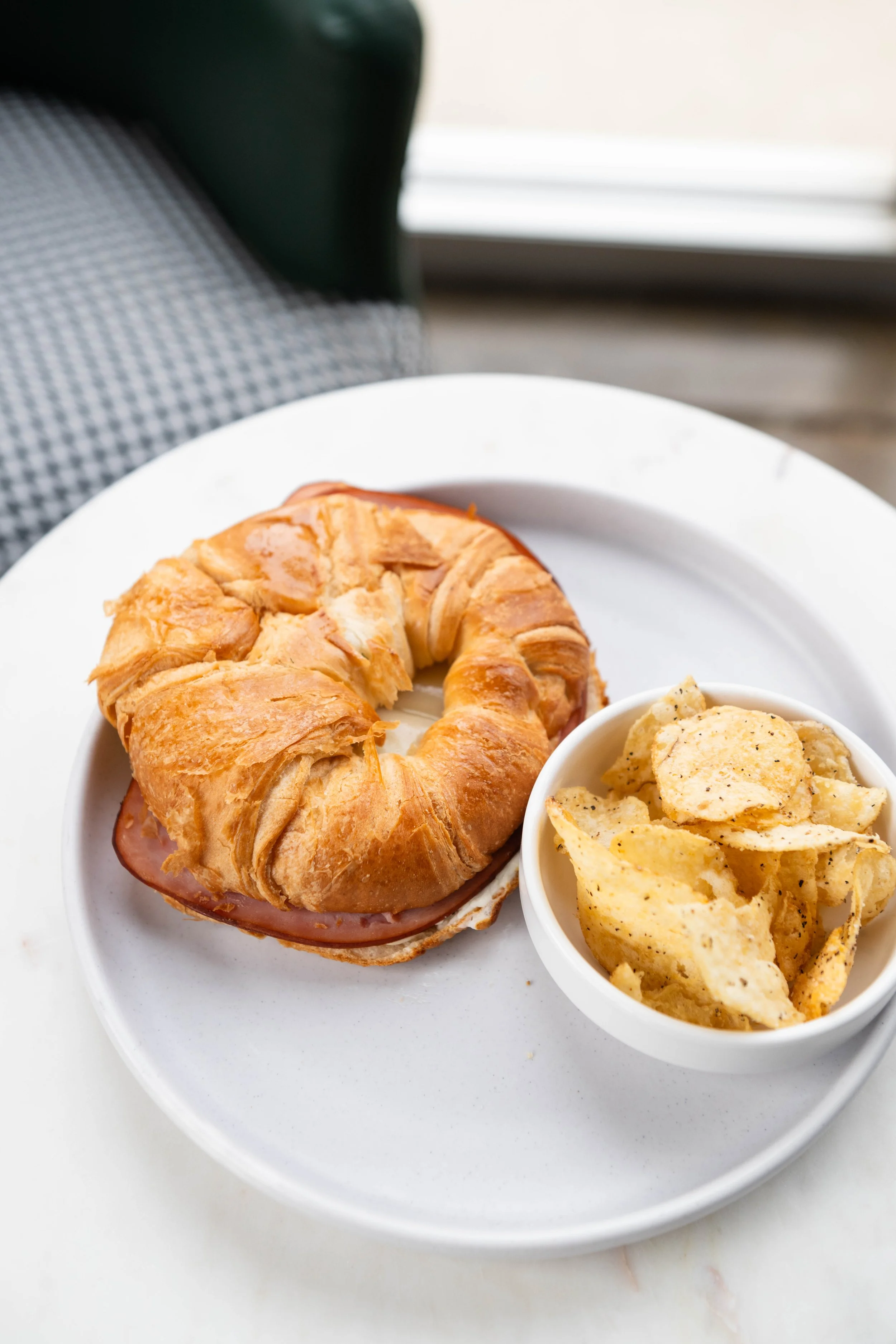 Croissant sandwich with ham and cheese served with potato chips on a white plate.
