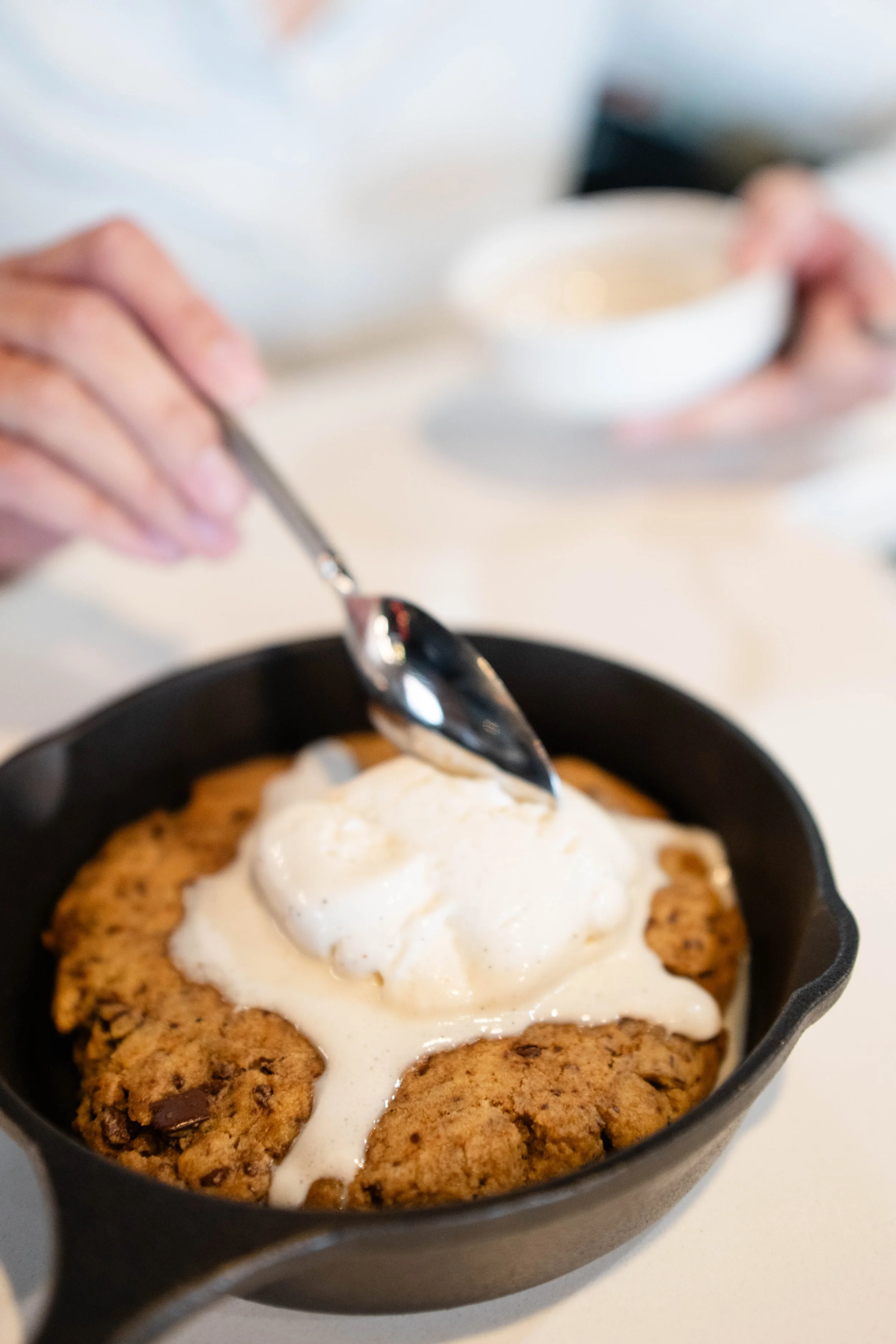 A freshly baked chocolate chip cookie topped with melting vanilla ice cream in a black cast iron skillet.