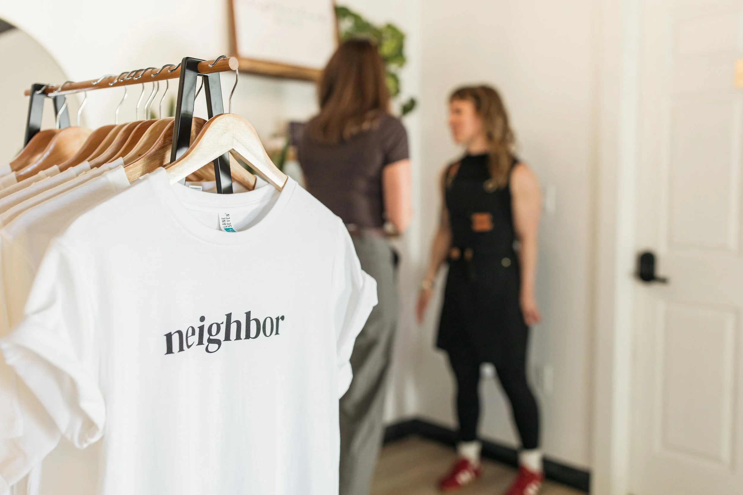 Neighborhood Wax branded T-shirts displayed inside the Denver waxing studio with team members in the background.