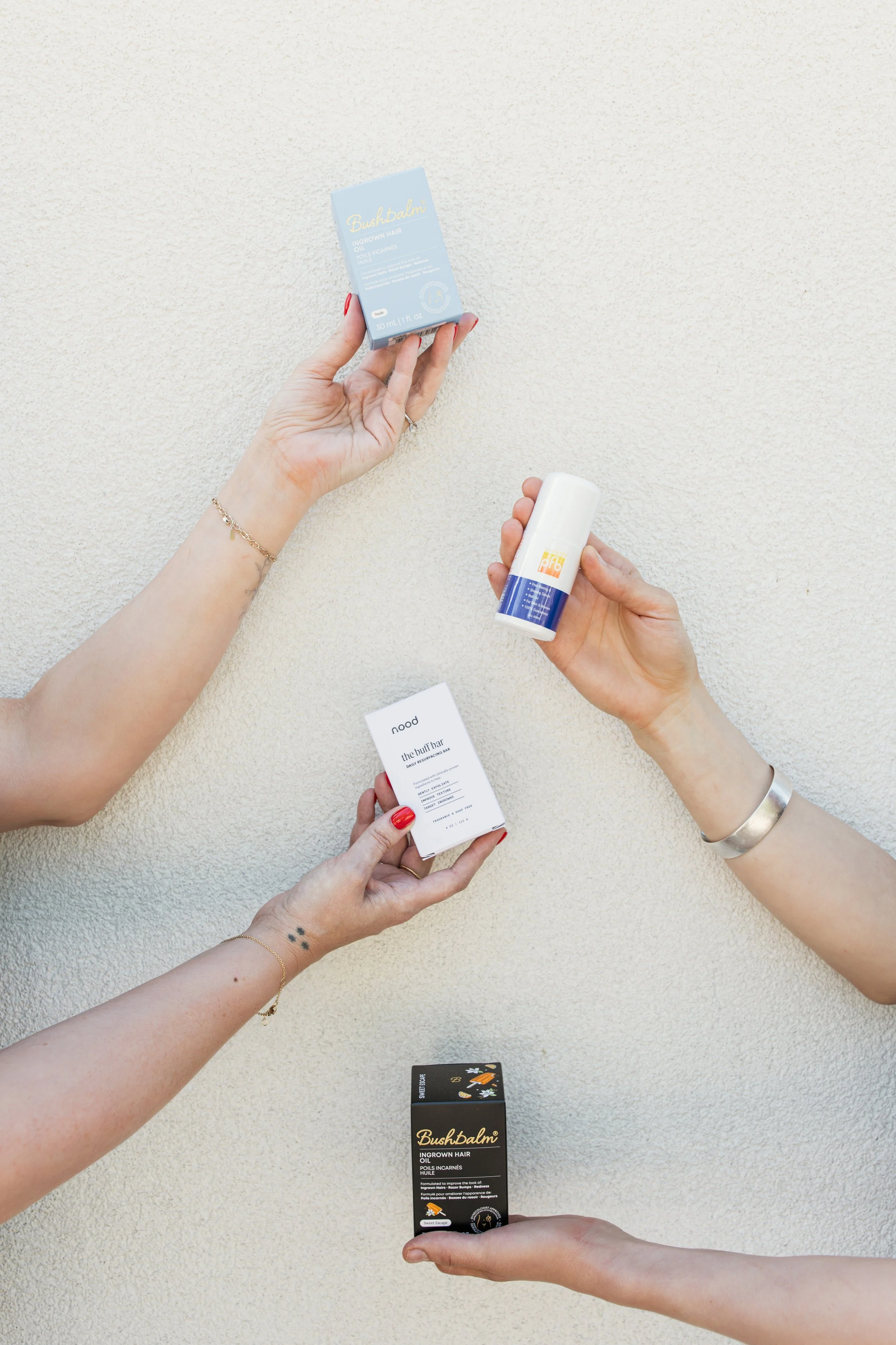 Hands displaying Bushbalm and other post-wax skincare products available at Neighborhood Wax