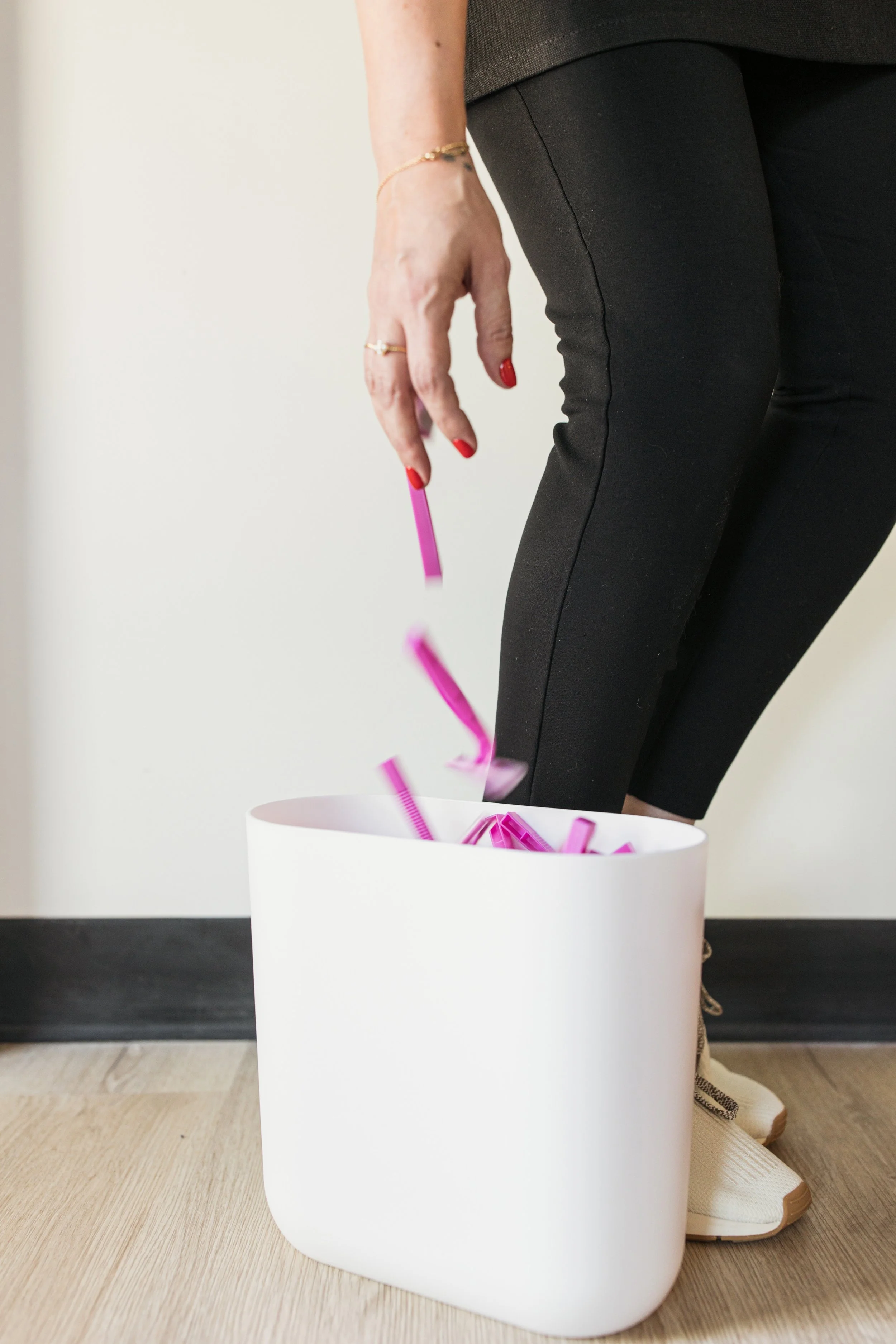 Woman dropping pink disposable razors into a trash bin, encouraging consistent waxing instead of shaving between appointments.