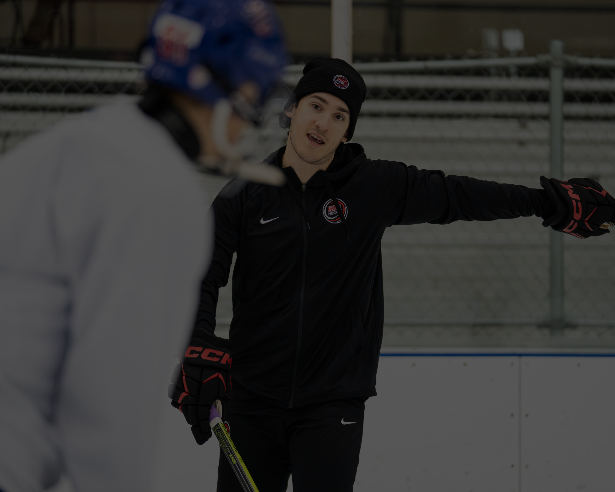 A hockey coach giving instructions to a player during practice on an ice rink.