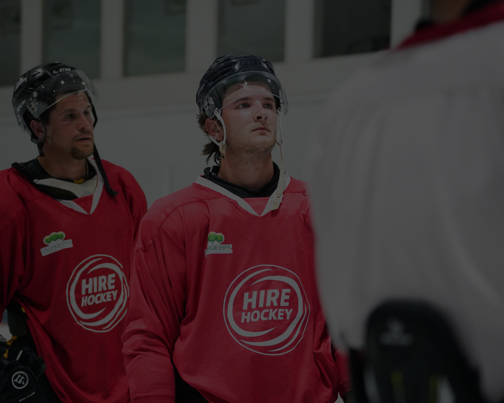 Ice hockey players wearing red jerseys with 'HIRE HOCKEY' logo and black helmets at an ice rink.