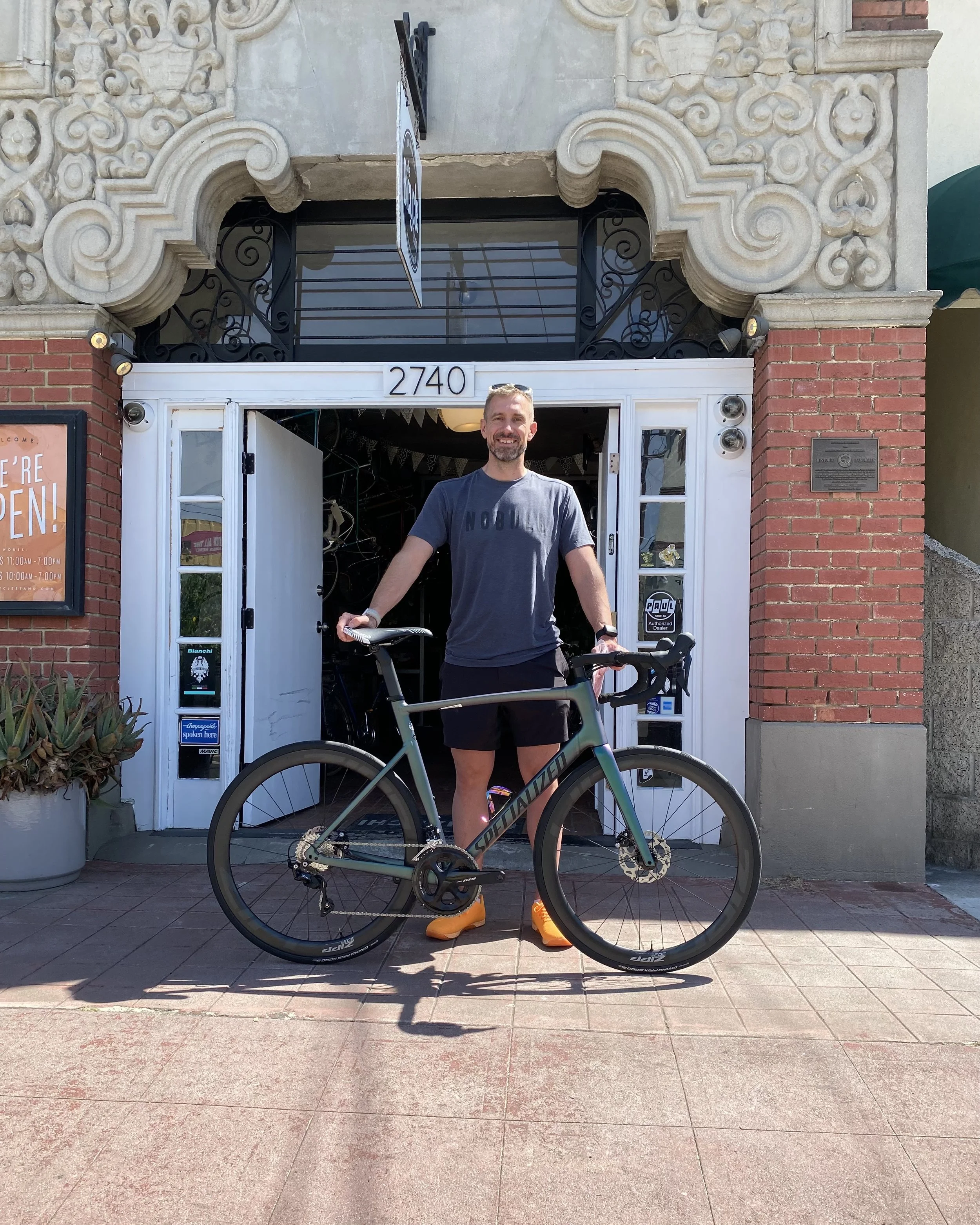 Man standing outside bike shop holding a bicycle in front of the entrance.