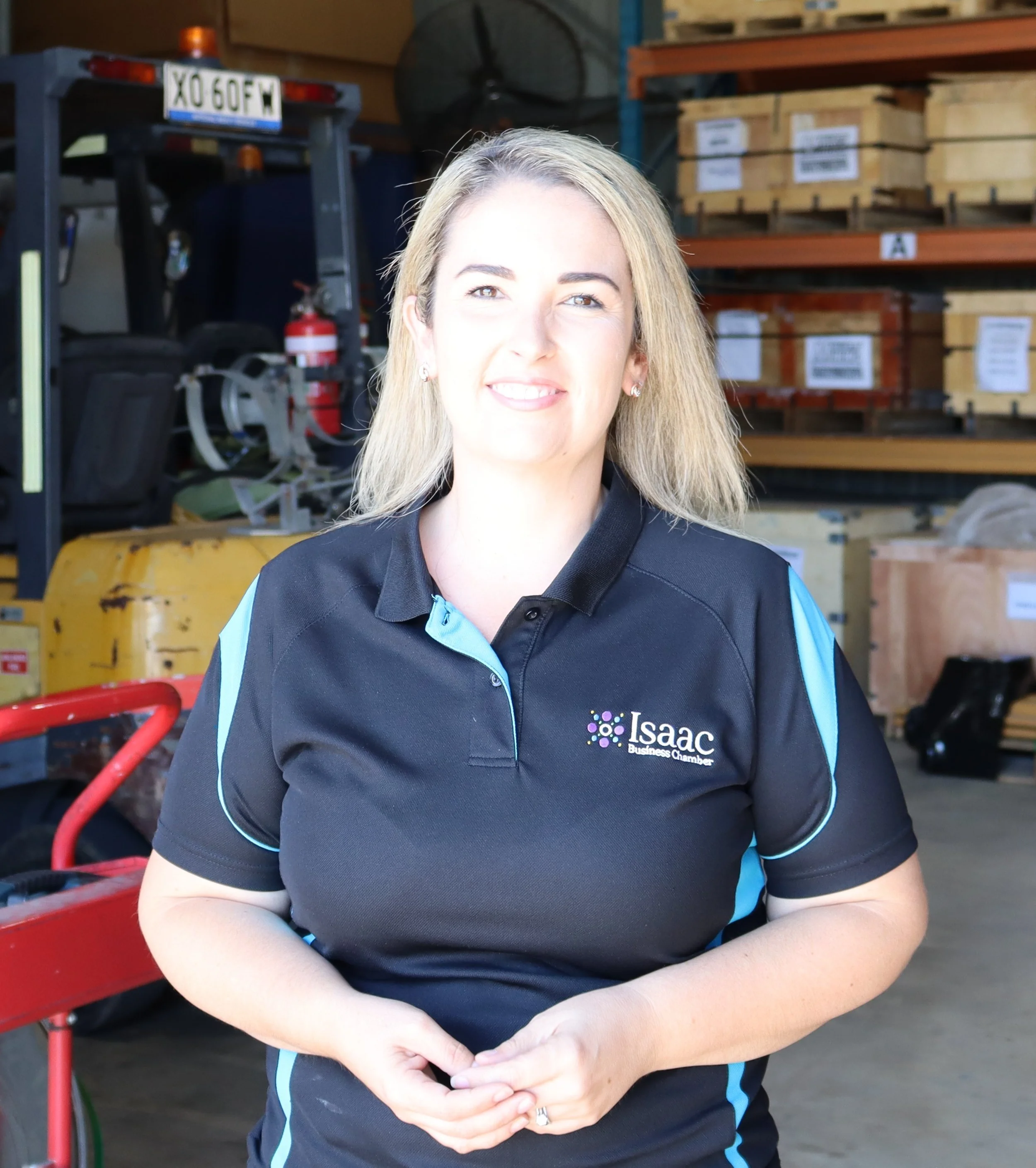 Close-up portrait of a smiling woman with light brown hair in a work uniform with "Salt Lake Milling Supply Solutions" logo, outdoors with greenery in the background.